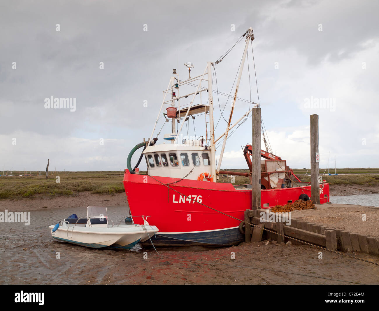 Rosso barca da pesca giacente sul fango a bassa marea Brancaster Staithe Norfolk in un giorno di pioggia Foto Stock