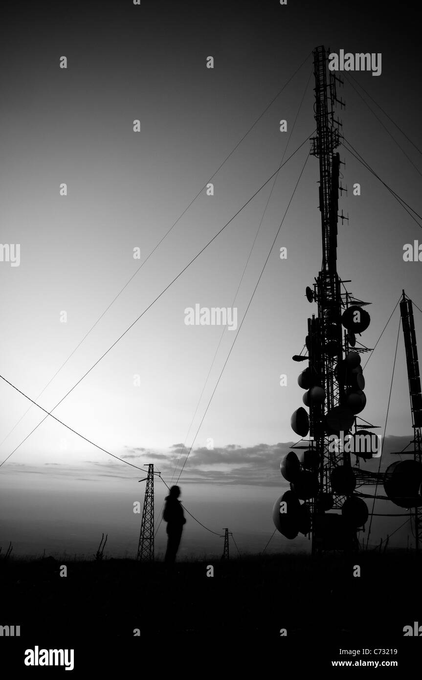 Silhouette di persona al tramonto vicino alle grandi antenne di montagna Foto Stock