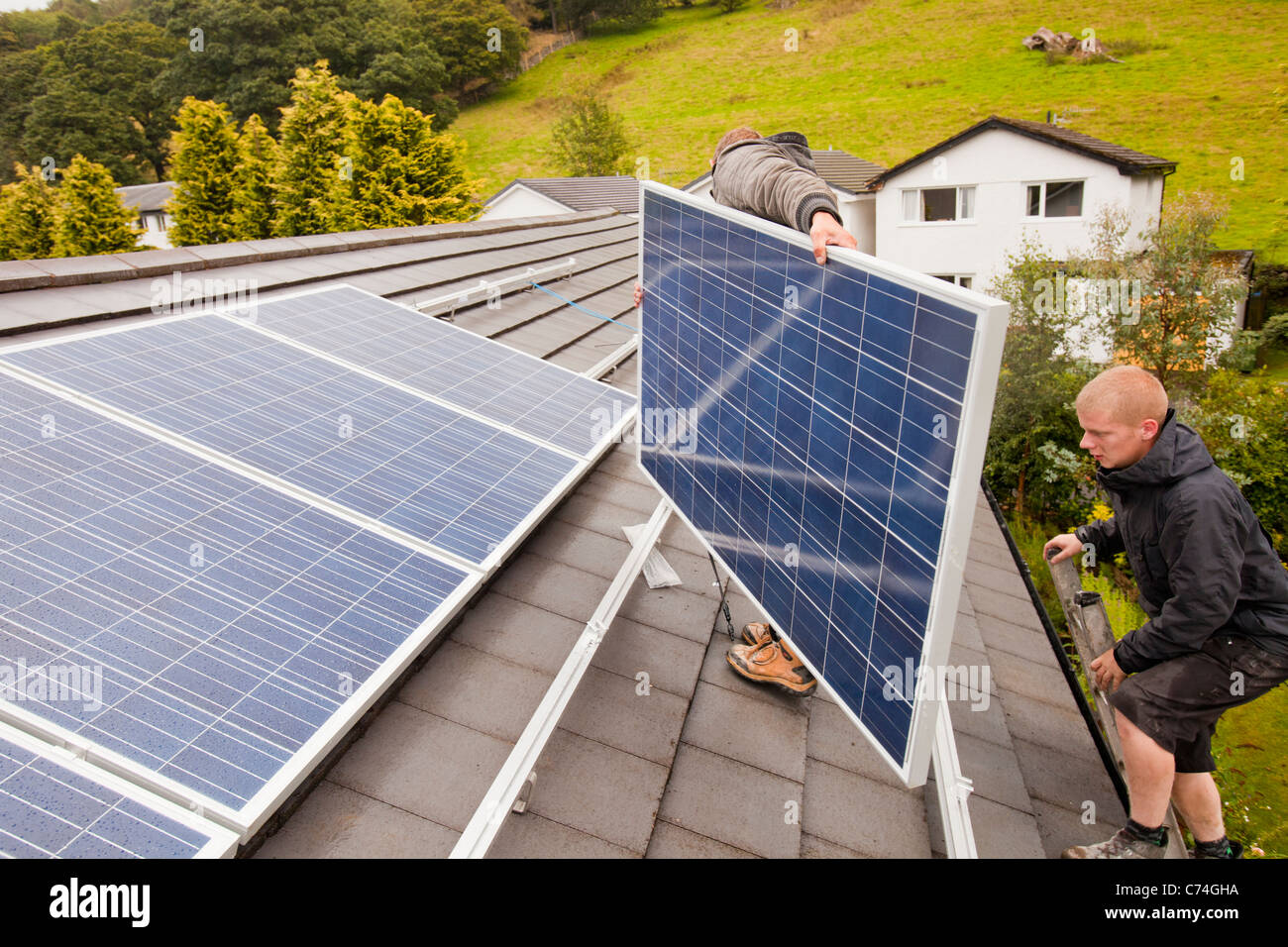 Lavoratori installazione solare pannelli elettrici su un tetto di casa a Ambleside, Regno Unito. Foto Stock