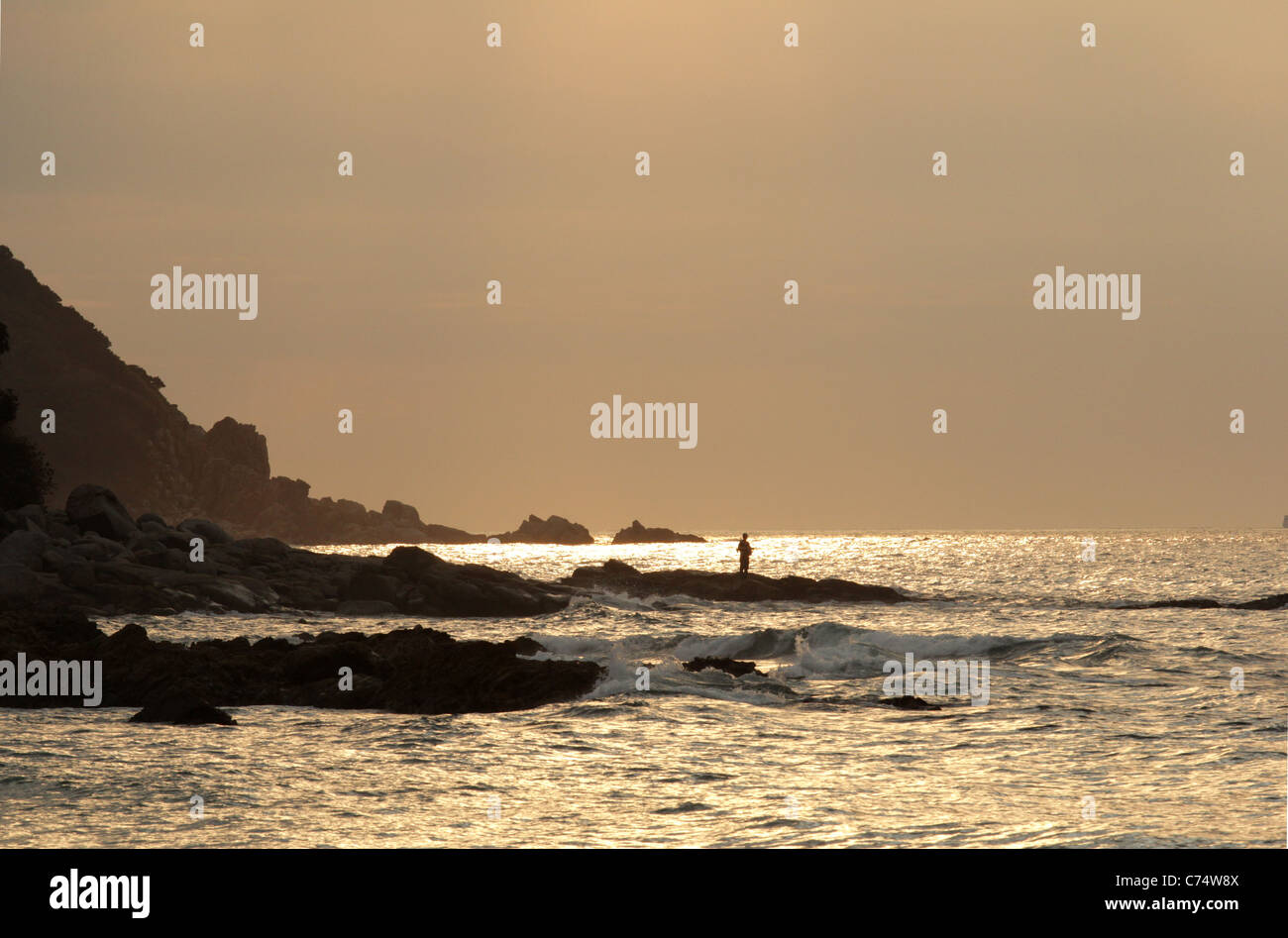 Tramonto sulla spiaggia e rocce con un uomo esca la pesca Foto Stock