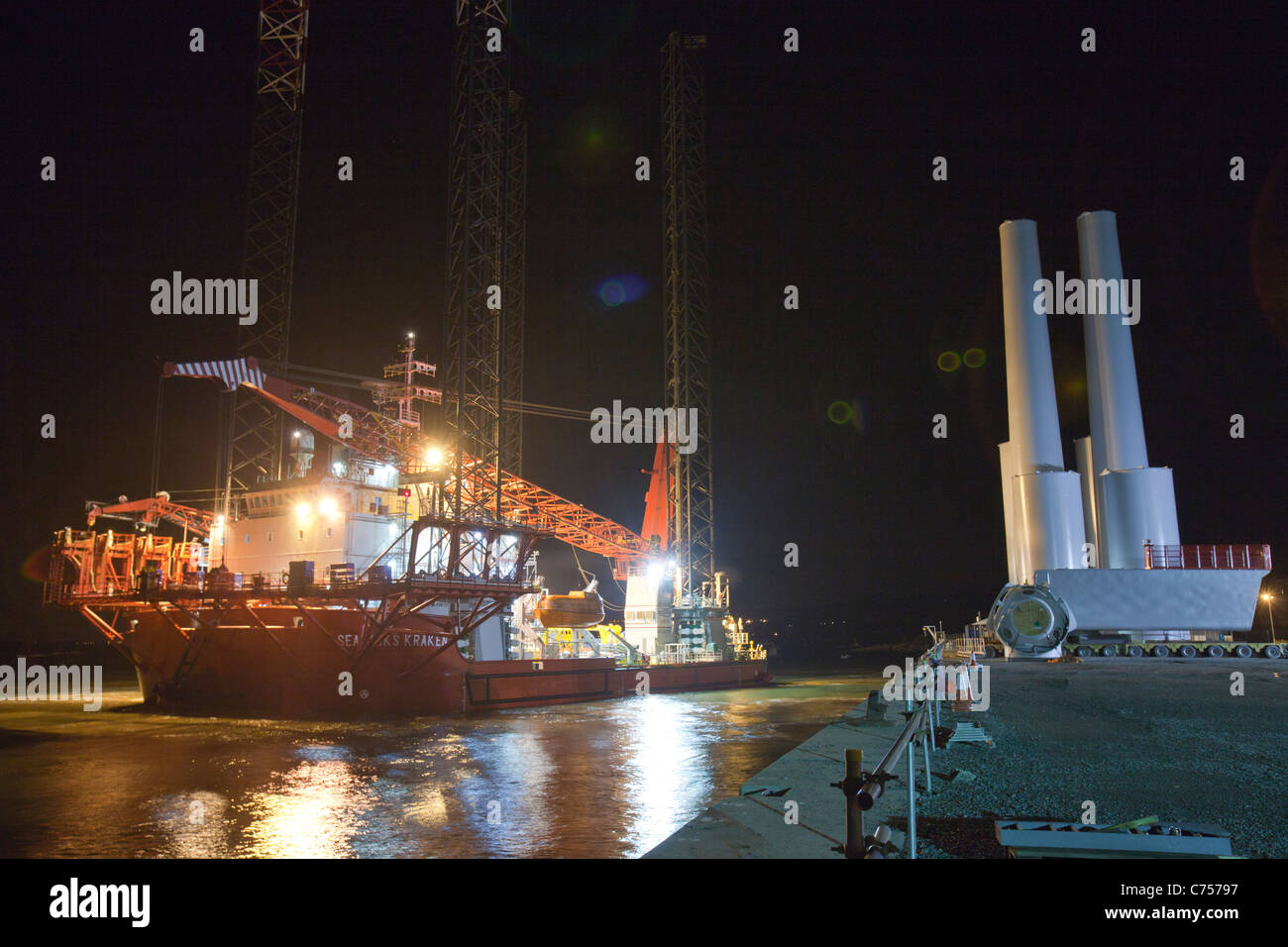 Un jack up barge essendo caricato con tutte le parti delle turbine di notte, per il Walney offshore wind farm Foto Stock