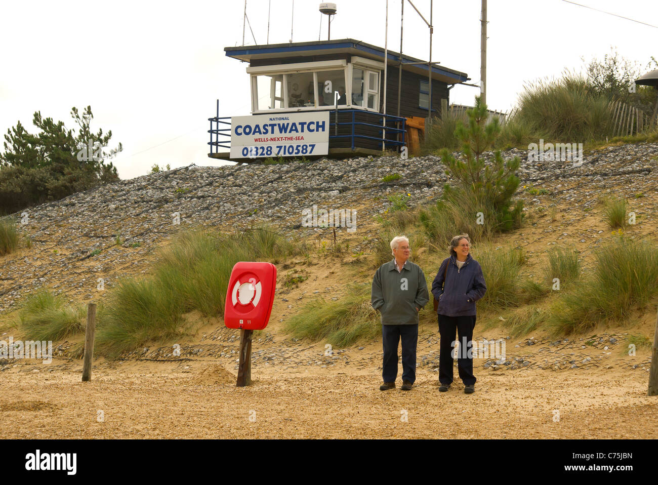 Un uomo e una donna che guarda verso il mare di fronte a presidiata Coastwatch nazionale stazione in pozzetti Norfolk Foto Stock