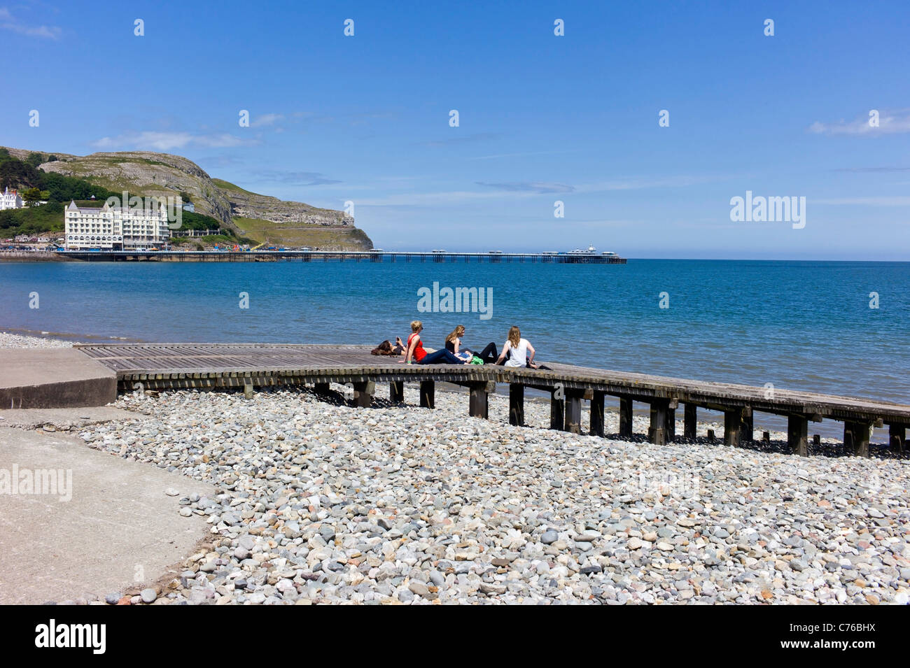 I giovani studenti di sesso femminile per i bagni di sole su un pontile in legno sul lungomare di Llandudno, sullo sfondo di un mare, pier, Great Orme con un cielo blu. Foto Stock