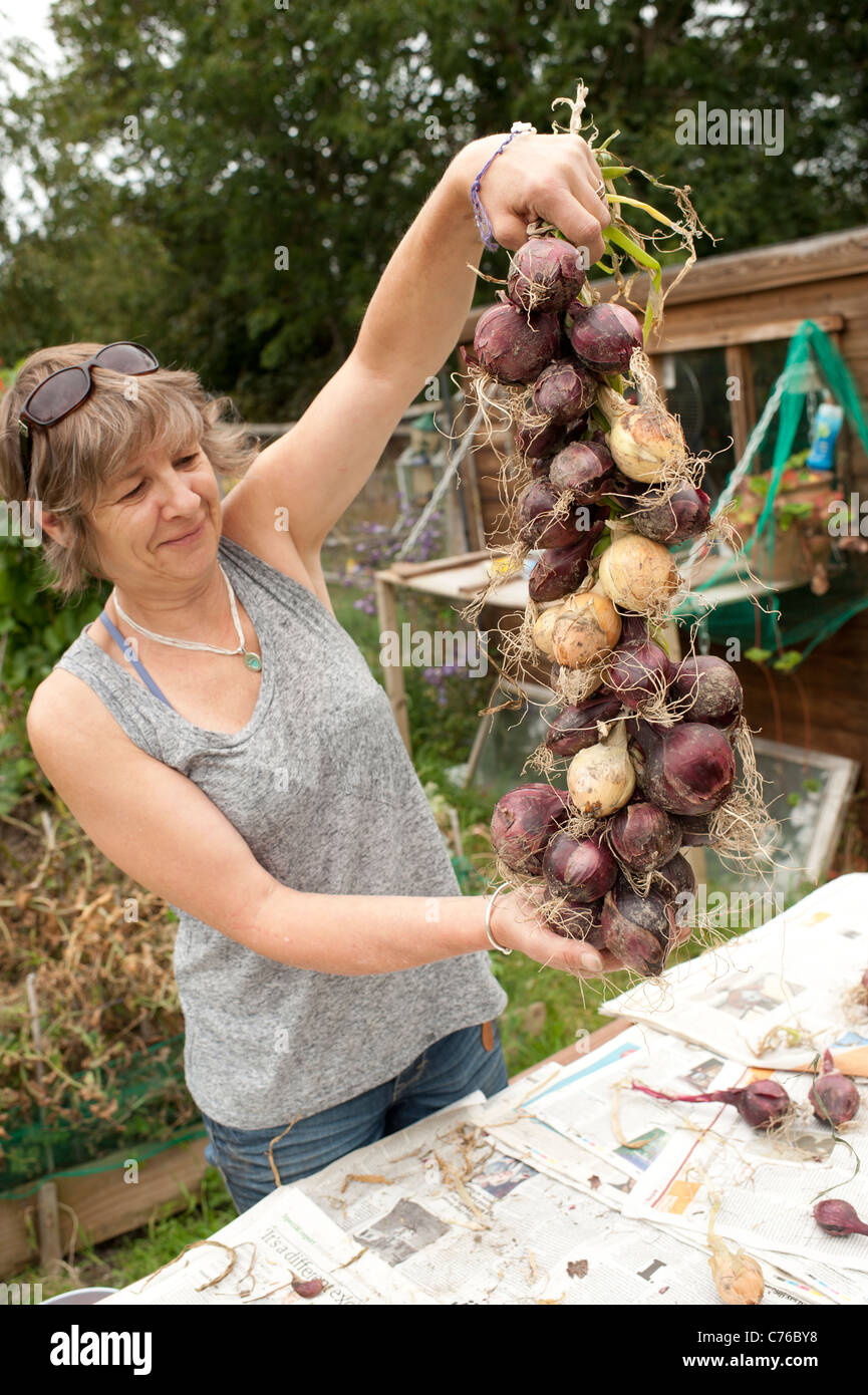 Una donna giardiniere con una stringa di cipolle che ella è cresciuta sul suo riparto garden, REGNO UNITO Foto Stock