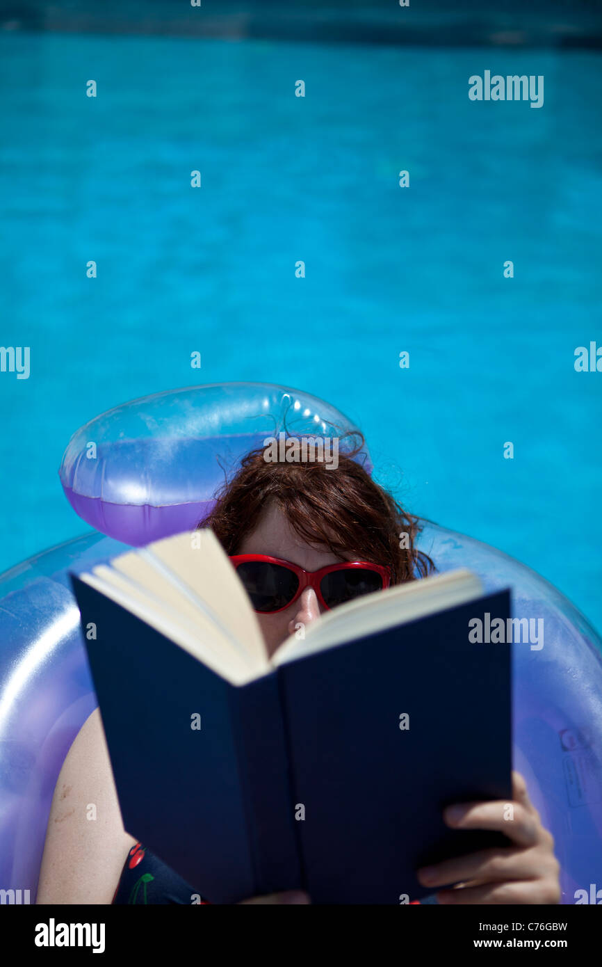 Donna libro lettura giacente su lilo in piscina. Foto Stock