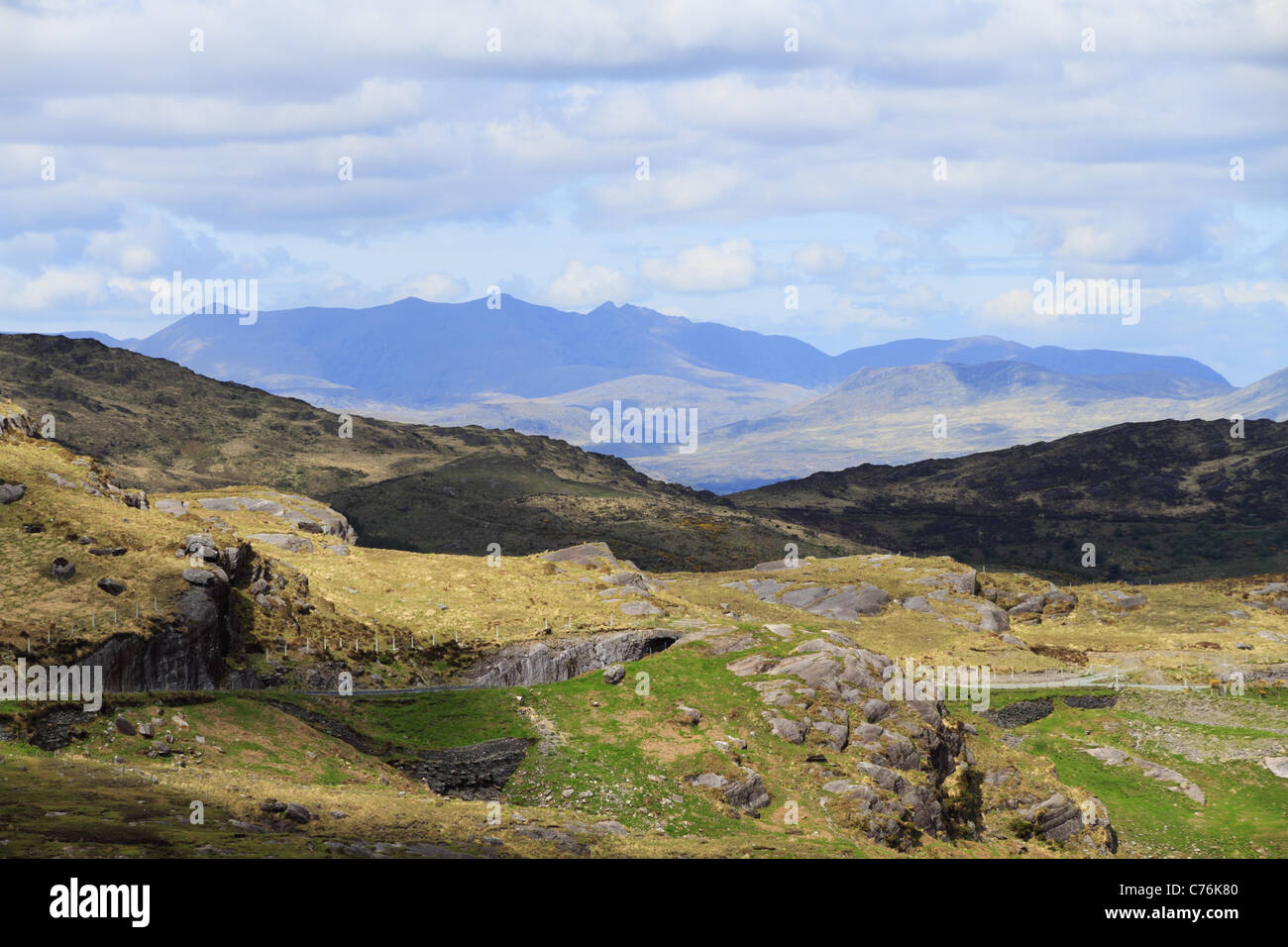 Una strada di montagna taglia attraverso le colline di Kerry, con il MacGillycuddy Reeks sullo sfondo le montagne più alte in Irlanda. Foto Stock
