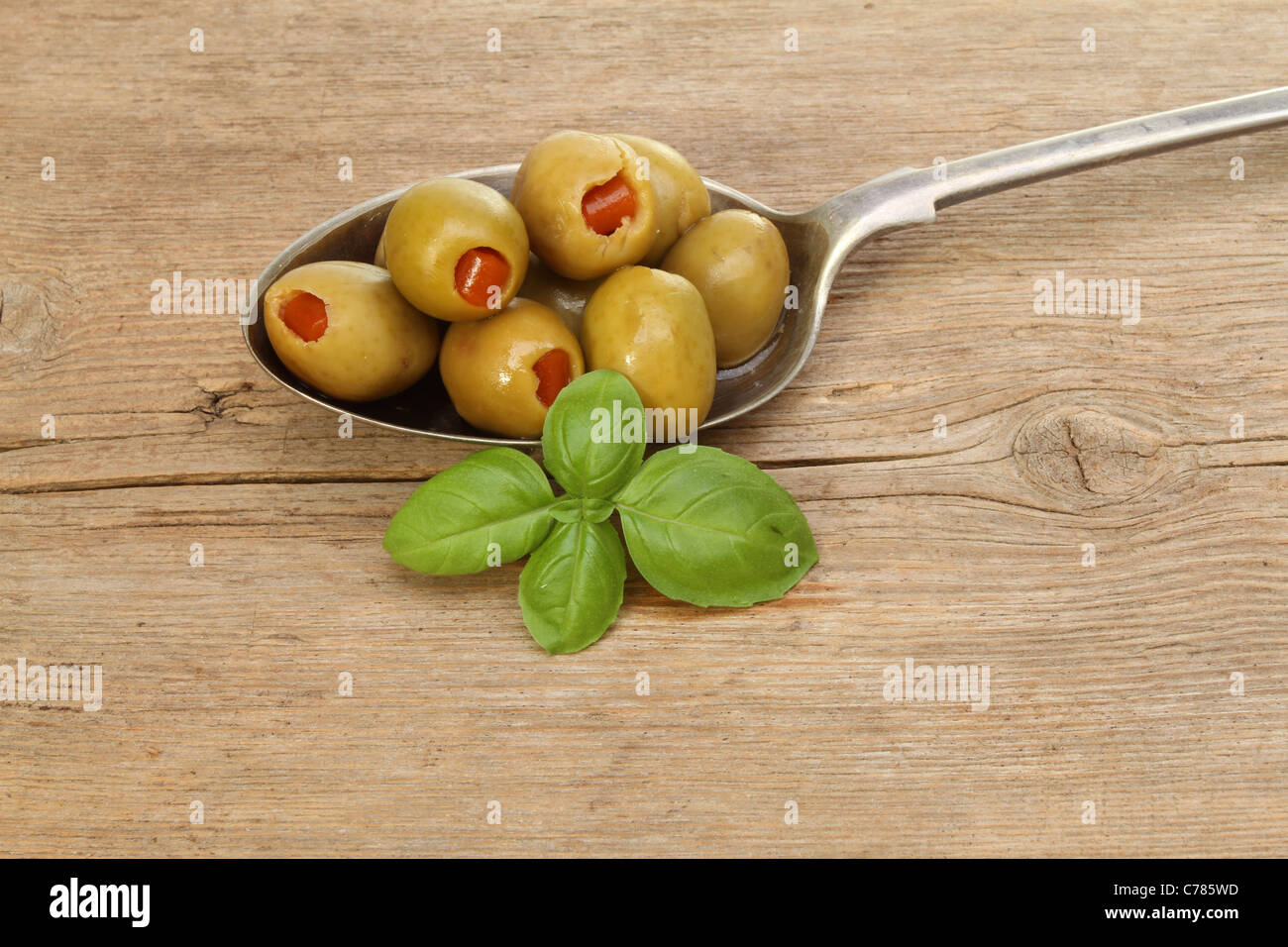 Olive farcite in cucchiaio d'argento con un rametto di basilico sul vecchio legno rustico Foto Stock
