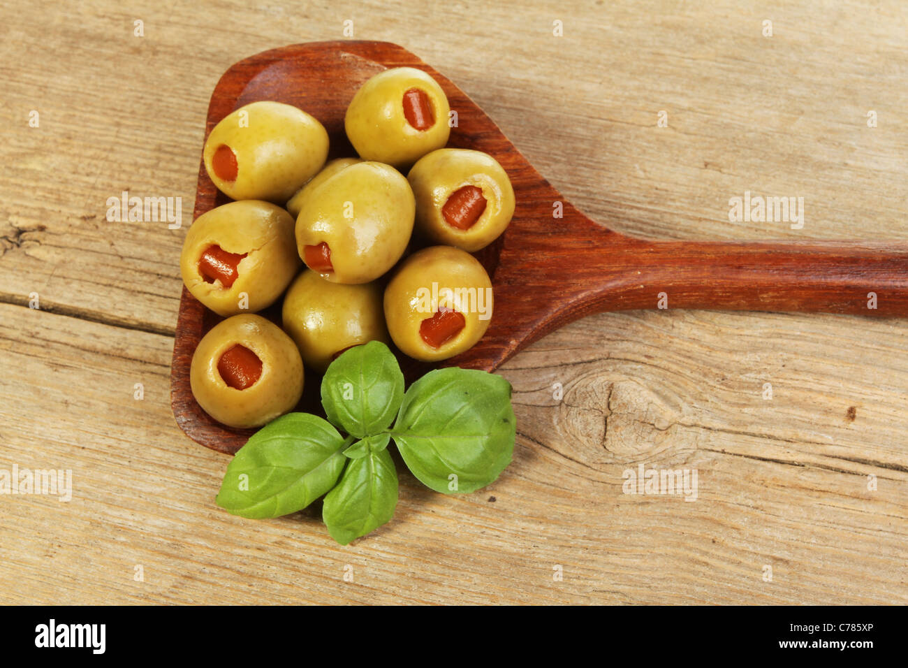 Le olive in un cucchiaio di legno con un rametto di basilico sul vecchio legno stagionato Foto Stock