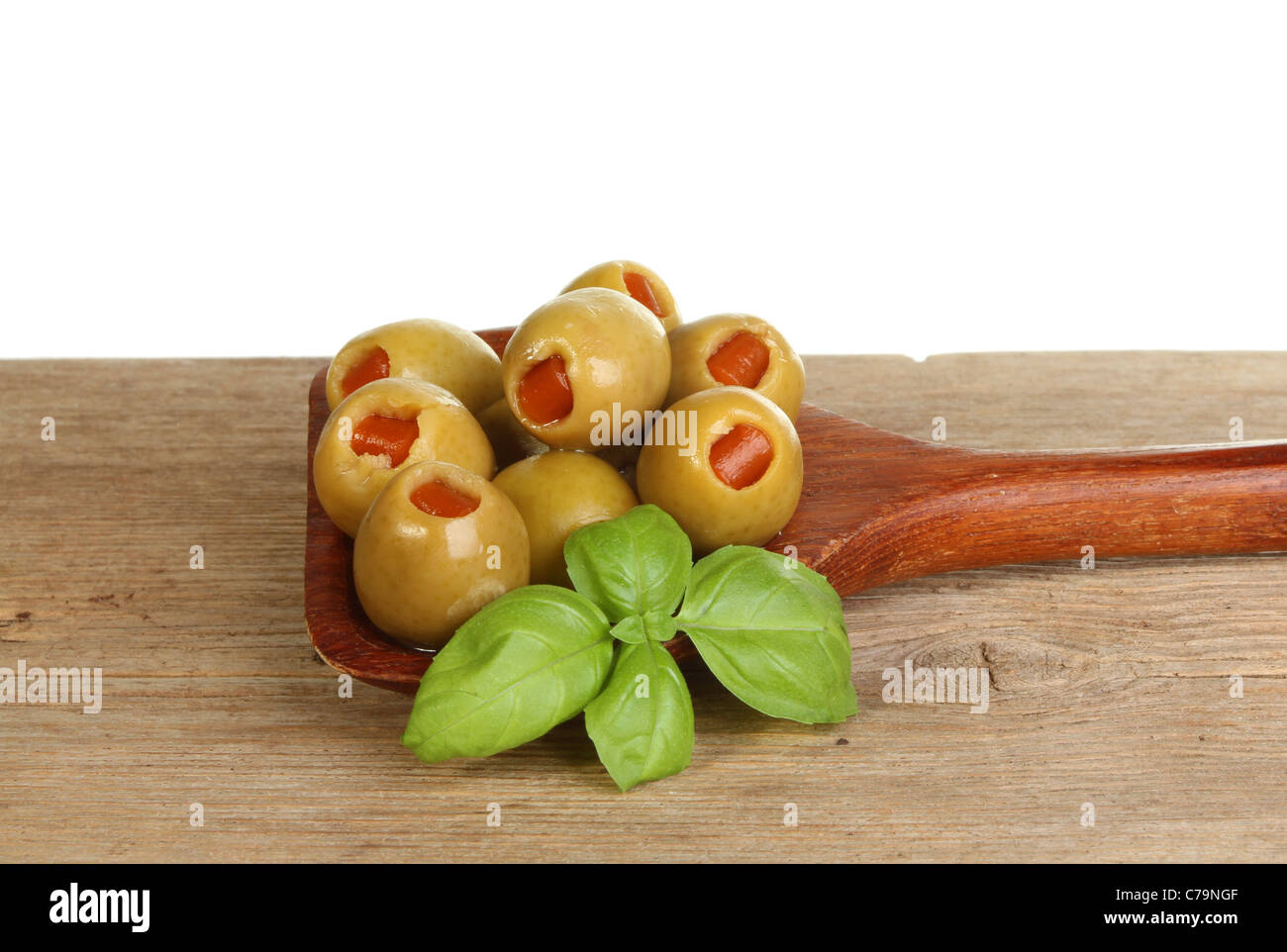 Le olive e un ciuffo di basilico fresco in un cucchiaio di legno sul vecchio legno stagionato contro uno sfondo bianco Foto Stock