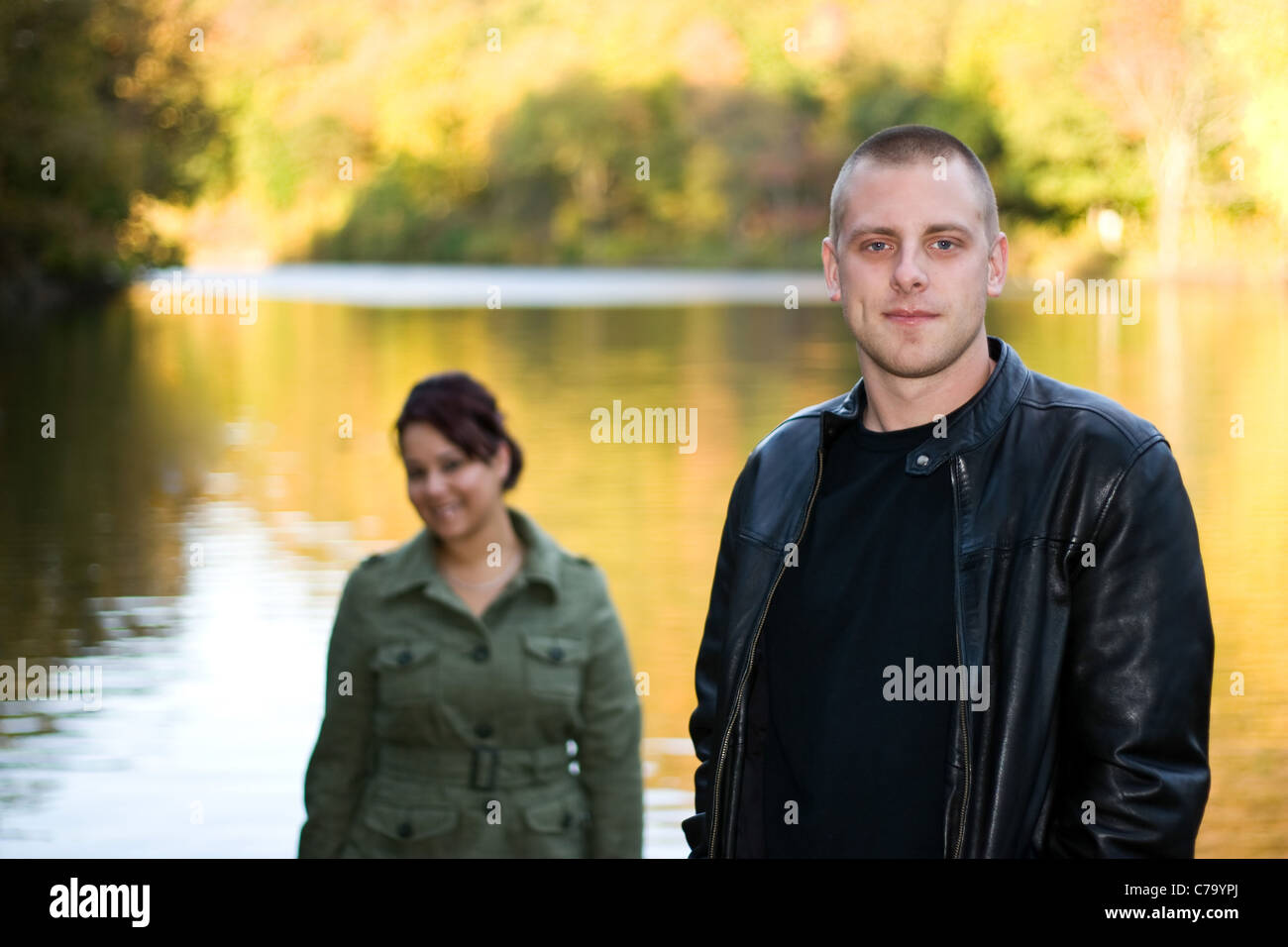 Una giovane coppia felice in piedi da un lago in autunno. Profondità di campo con il focus sull'uomo in primo piano. Foto Stock