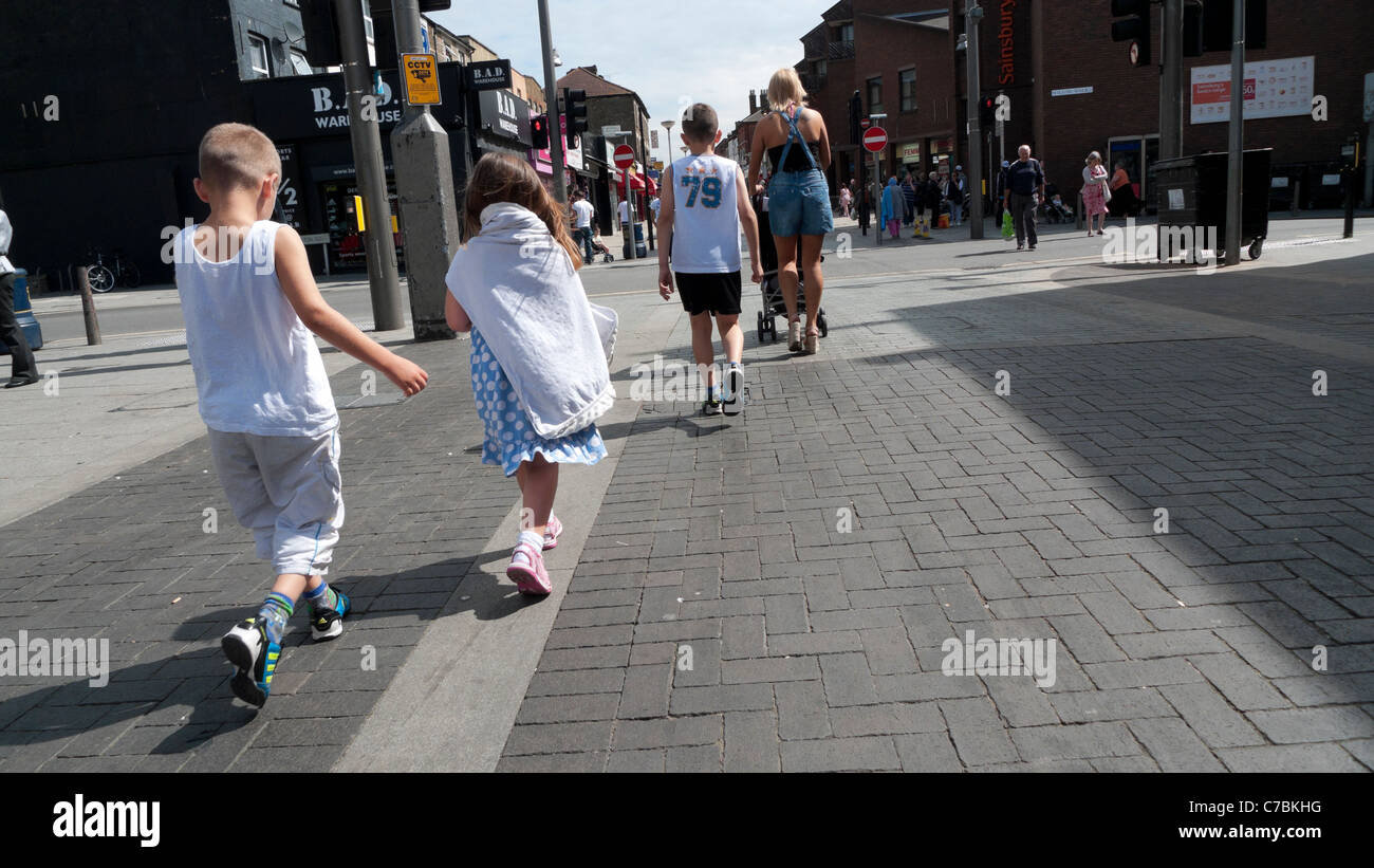 Vista posteriore della madre e bambini durante le vacanze estive per fare shopping a piedi lungo high street Walthamstow England Regno Unito Foto Stock
