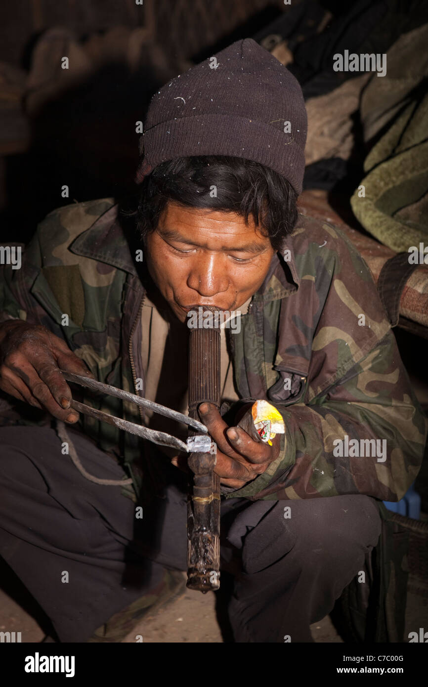 India, Nagaland, Longwa, Oppio Den, Konyak Naga uomo applicando ember a luce tubo di oppio Foto Stock