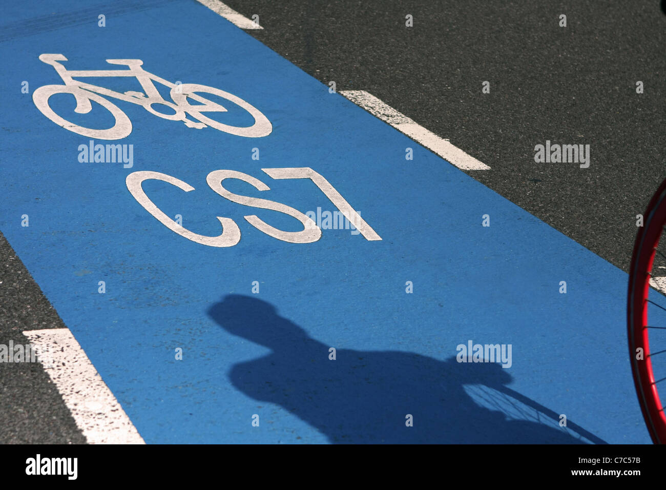 Un ciclista's shadow e parte del suo ciclo di ruota anteriore come egli cicli in un ciclo di blu corsia autostradale Foto Stock