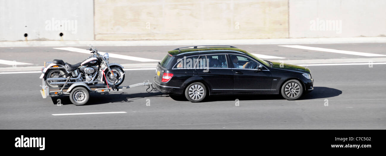Vista laterale conducente in rimorchio di rimorchio di automobile nero caricato con moto che guida lungo la strada di autostrada M25 Essex Inghilterra Regno Unito Foto Stock
