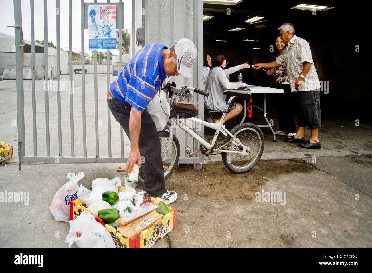 Un americano africano uomo pacchi cibo donato a un ente di beneficenza distribuzione in Santa Ana CA per riportare a casa su una bicicletta. Foto Stock