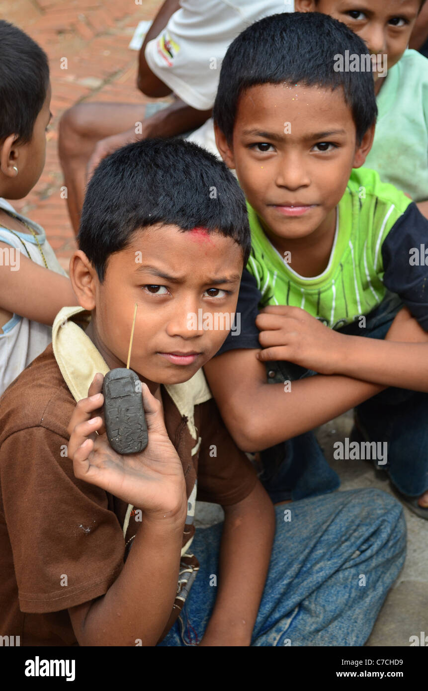 Ragazzi sit in strada, mostrando un "cellulare" hanno creato da argilla e uno stuzzicadenti, Bhaktapur, Nepal. Foto Stock