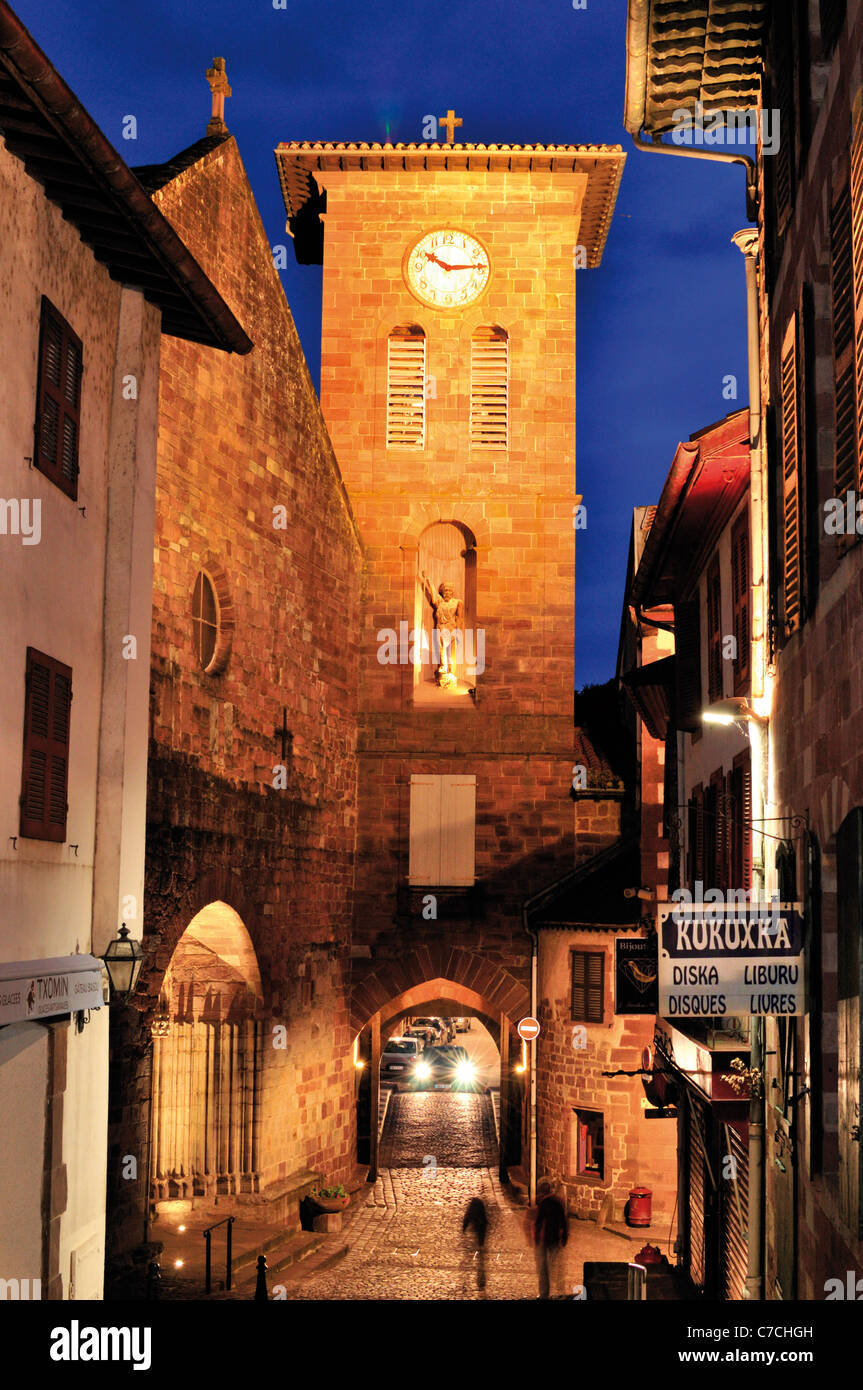 Francia, St. James modo: orologio notturno illuminato Rue de la Citadelle e Eglise Notre Dames in San Jean-Pied-de-Port Foto Stock