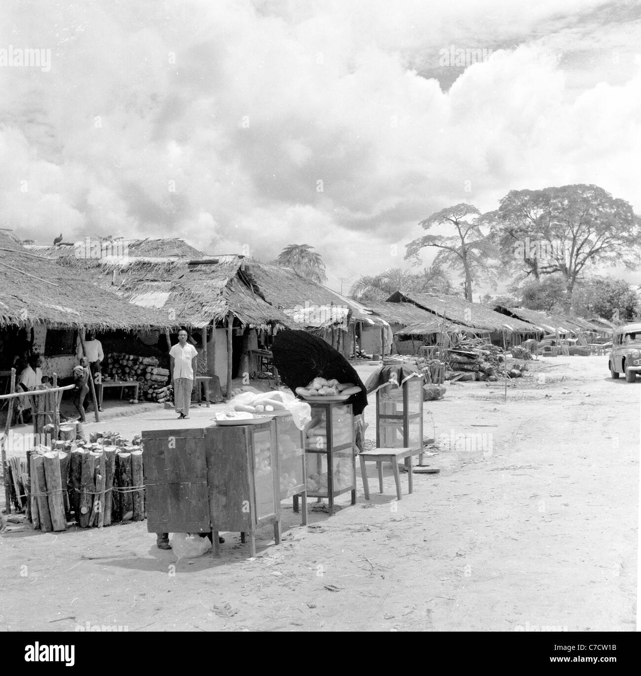 Nigeria, Africa, anni '50, quadro storico di capanne o baracche coperte e aperte di basso livello che vendono ceppi di legno e altre disposizioni. Foto Stock