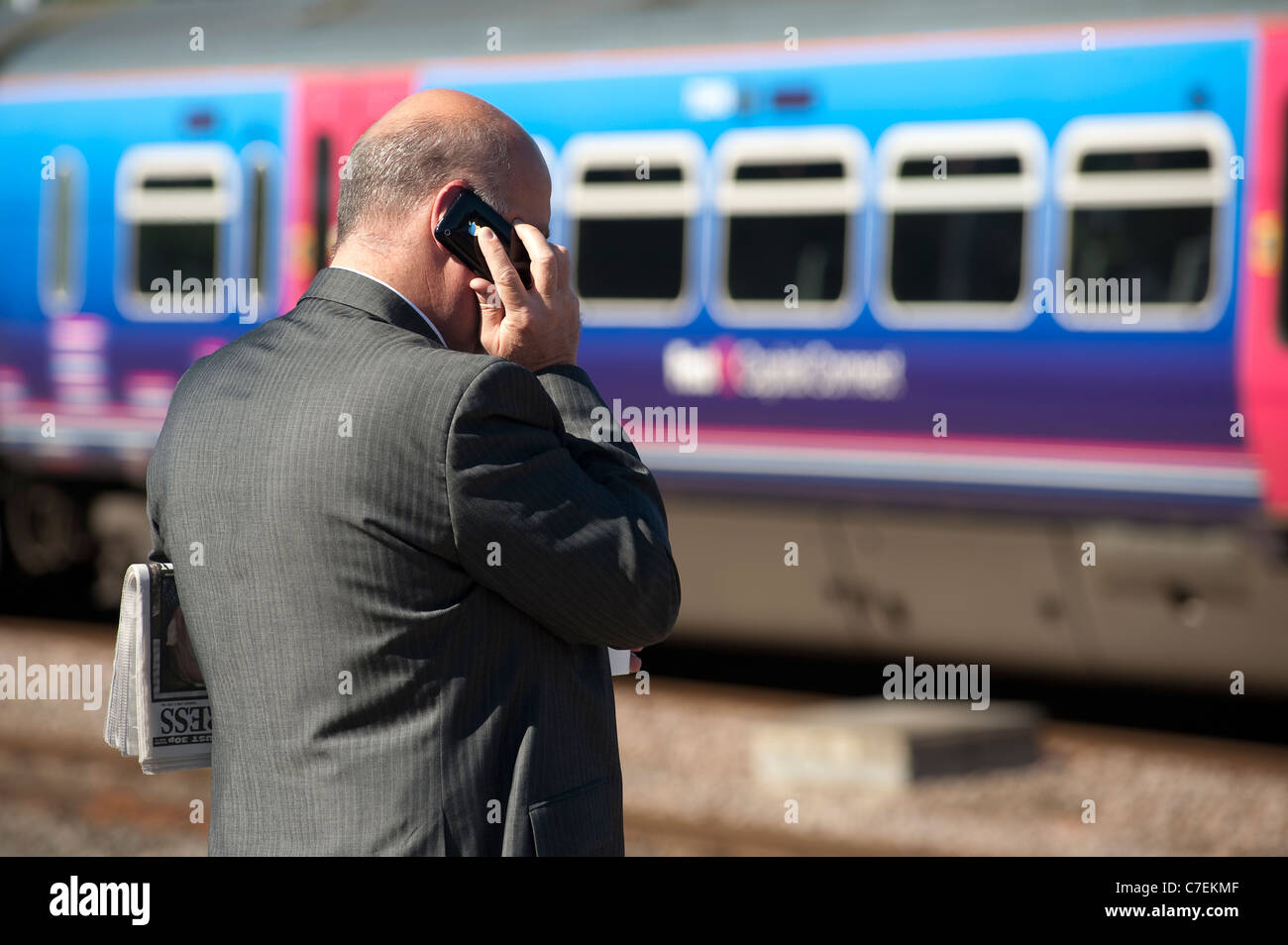 Imprenditore utilizzando un telefono cellulare in attesa di una stazione ferroviaria piattaforma. Foto Stock