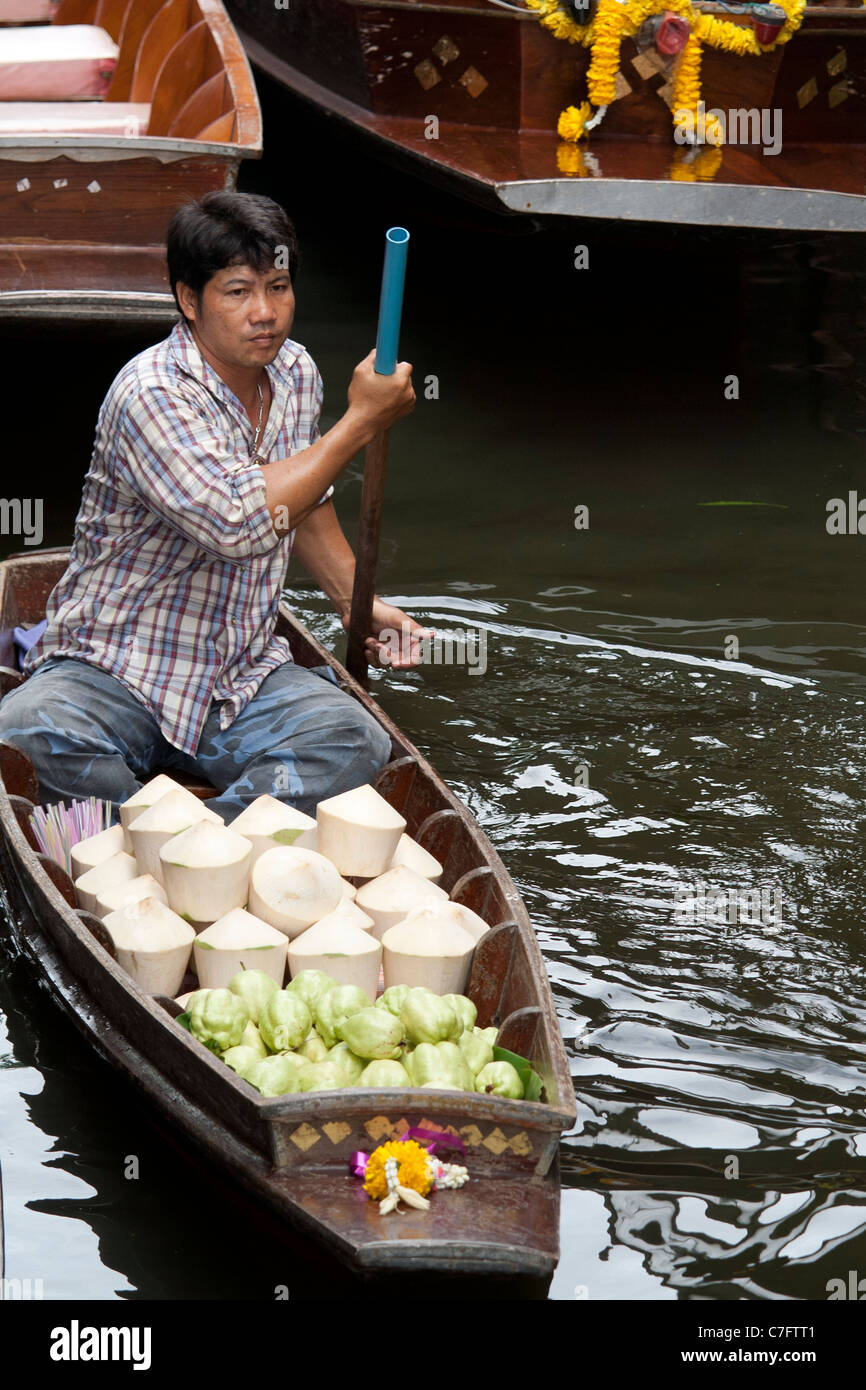 Una noce di cocco e star fruit venditore il canottaggio la sua barca presso il Dameon Saduk mercato galleggiante vicino a Bangkok, Thailandia. Foto Stock