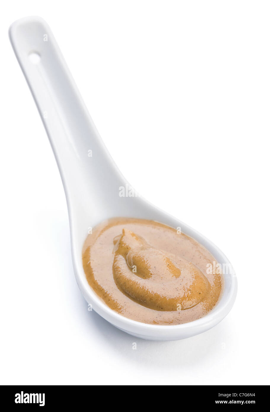Giallo senape salsa in cucchiaio di ceramica su bianco Foto Stock