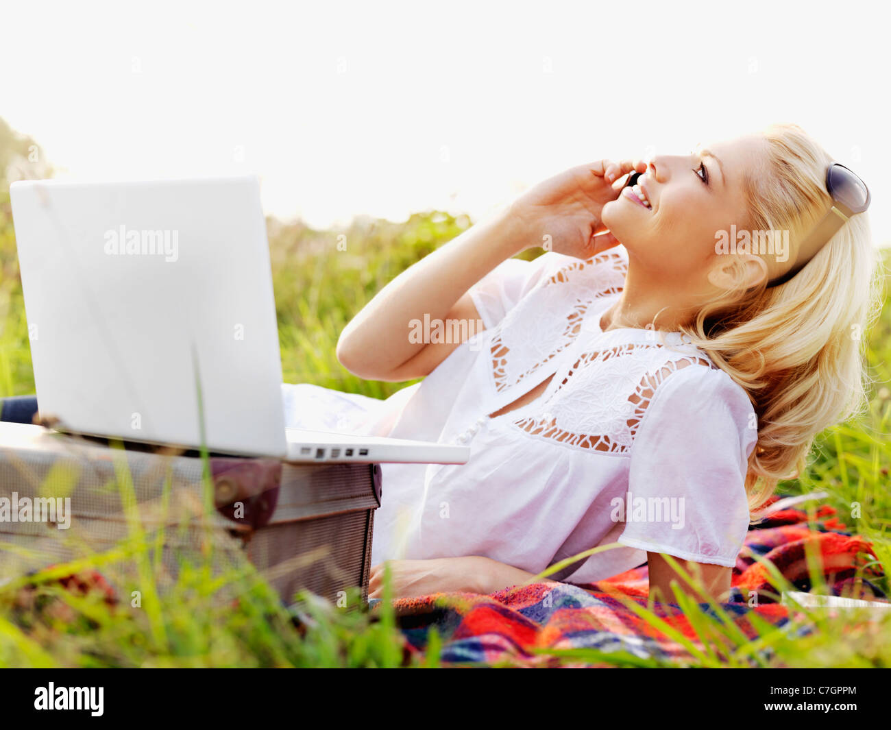 Una donna in natura con un computer portatile aperto e utilizzando un telefono cellulare Foto Stock