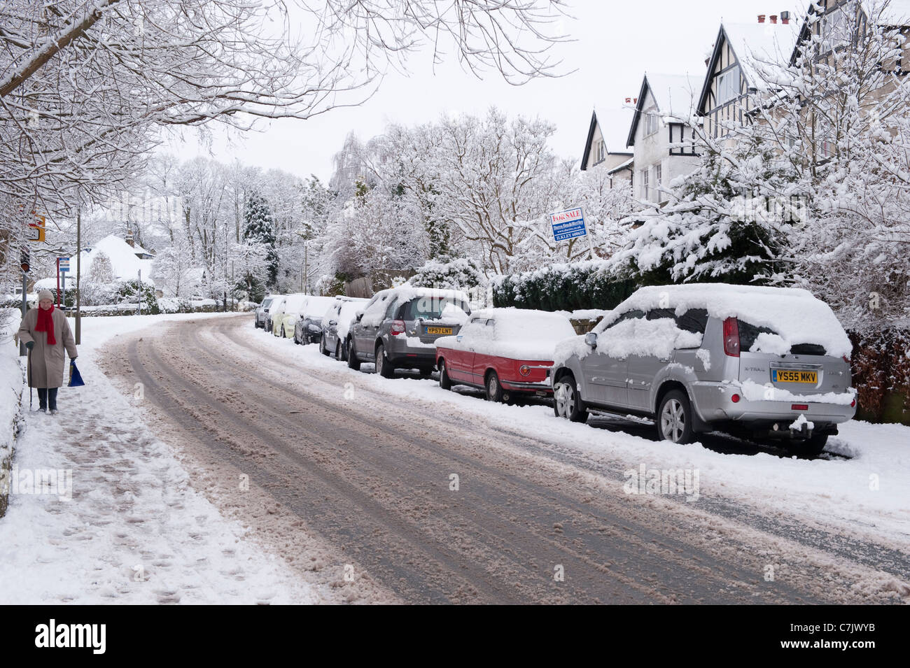 Strada invernale del villaggio (piste su strada coperta di neve, auto parcheggiate, pedonale a piedi, impronte su marciapiede) - Burley a Wharfedale, Inghilterra, GB, UK. Foto Stock