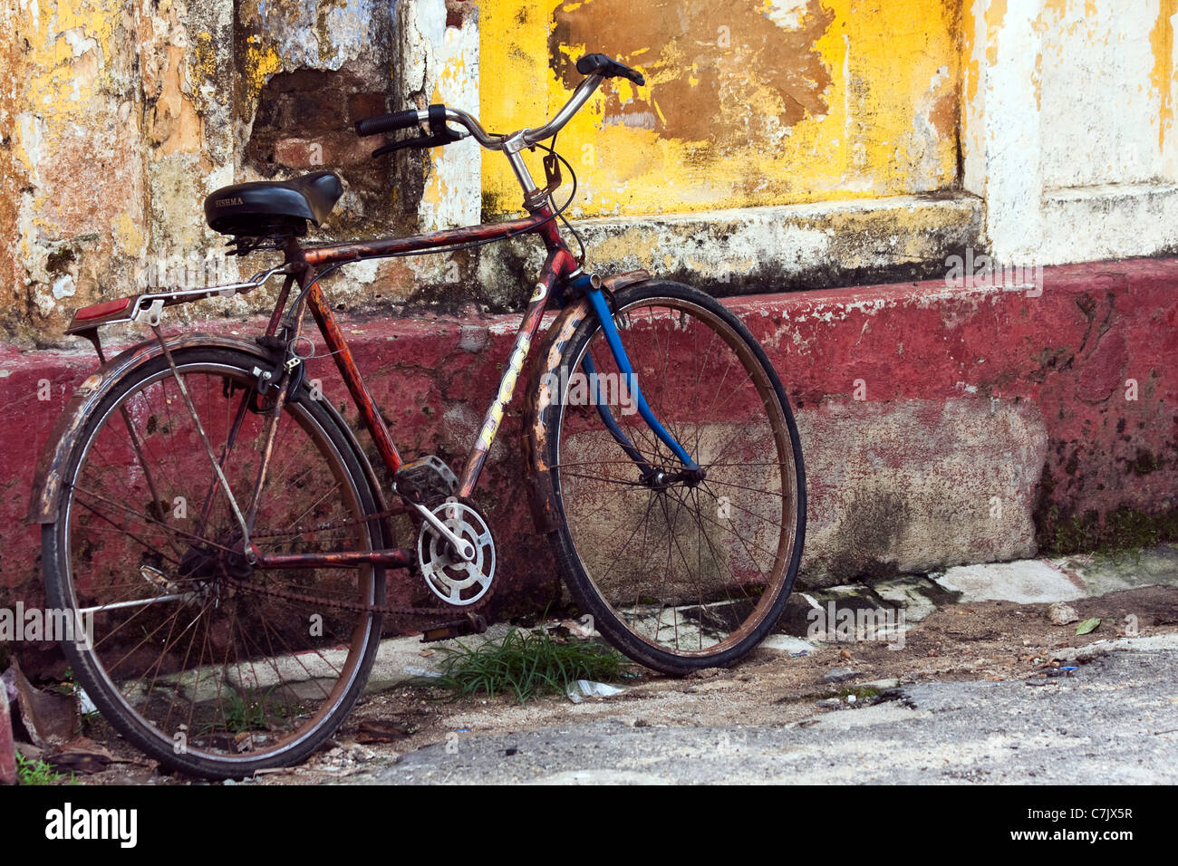Vecchio arrugginito moto parcheggiata fino contro una parete colorata su una delle strade a Galle, Sri Lanka Foto Stock