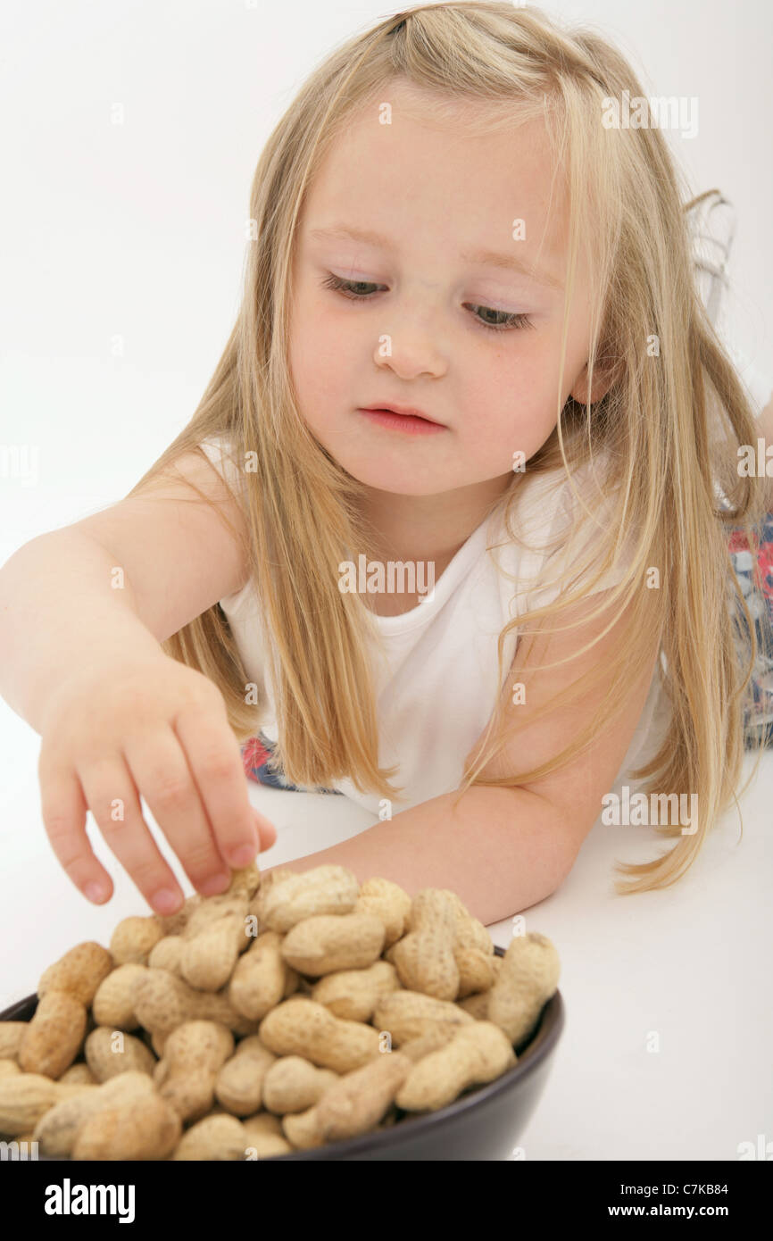 Un giovane bambino sdraiato per raggiungere una ciotola di dadi di scimmia. Foto Stock