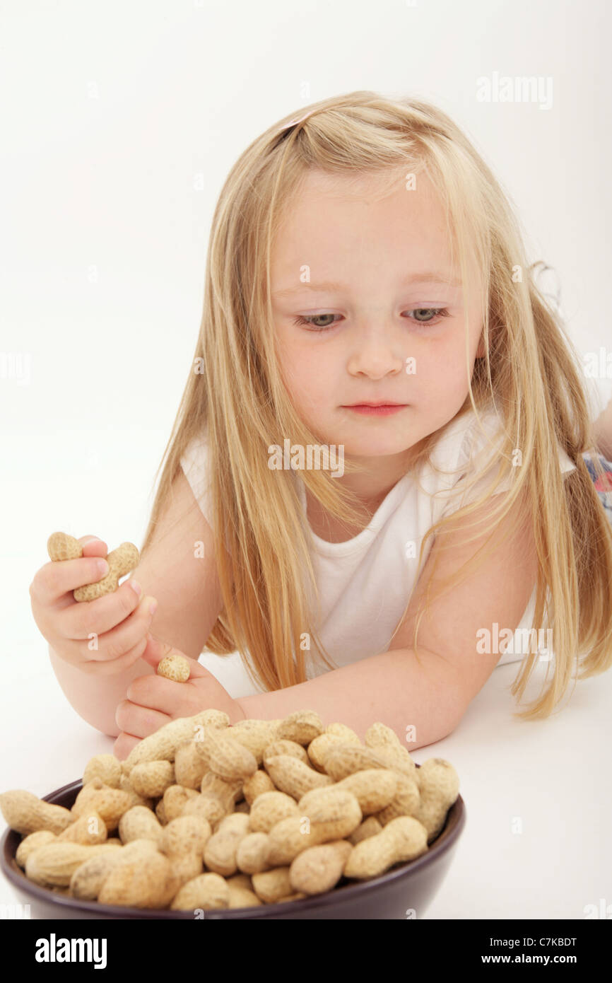 Un giovane bambino sdraiato per raggiungere una ciotola di dadi di scimmia. Foto Stock