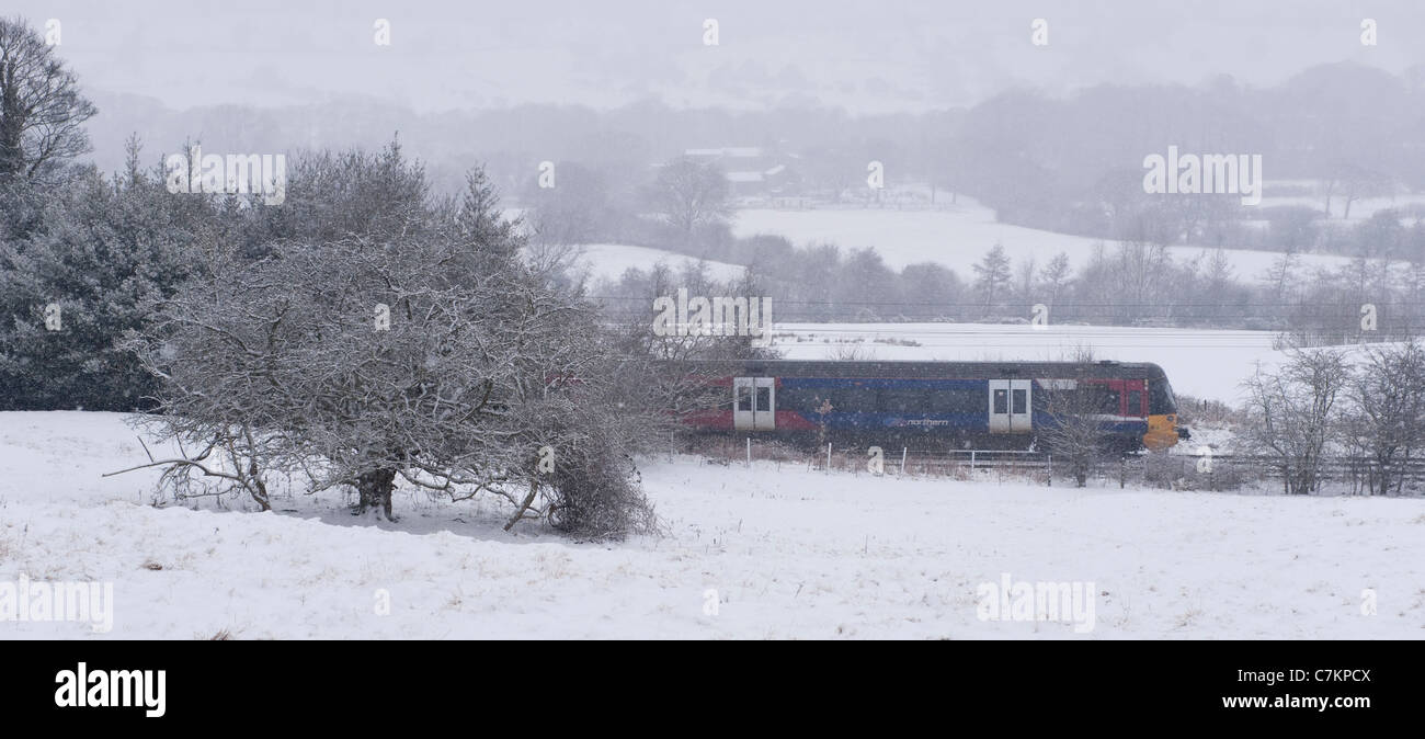 Neve che cade in nevosa giornata invernale e treno ferroviario locale passeggeri che viaggia attraverso i bianchi campi rurali - linea Wharfedale, West Yorkshire, Inghilterra, Regno Unito. Foto Stock