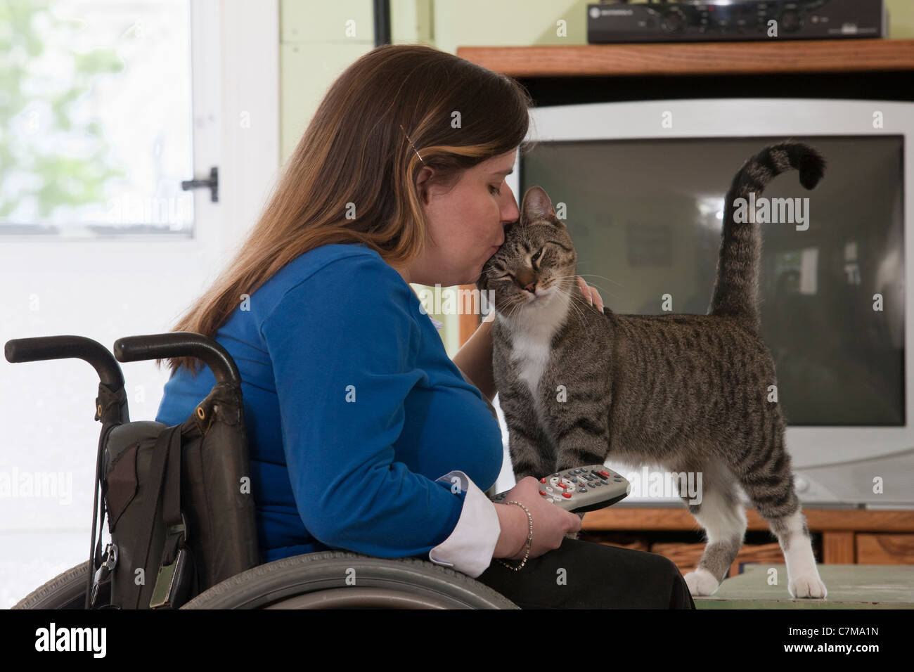 Donna con la spina bifida in una sedia a rotelle la bacia cat tenendo premuto il telecomando della TV Foto Stock