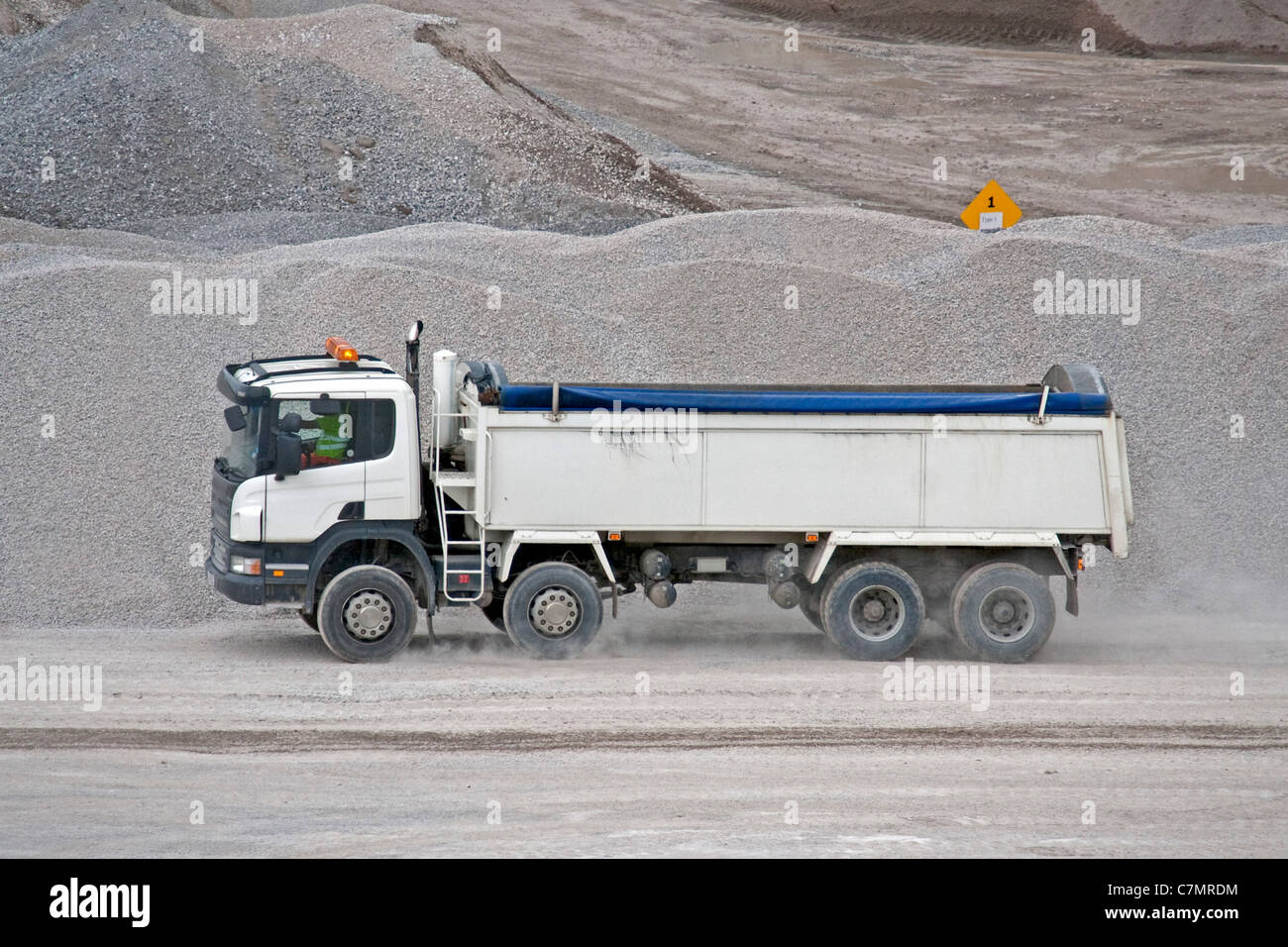 Un dumper ribaltabile bianco a 8 ruote viene mostrato durante il processo di raccolta di un carico di pietra da una cava. I dumper ribaltabili sono comunemente utilizzati nelle costruzioni e nelle miniere per il trasporto di materiali sfusi come pietra, ghiaia e sabbia. Foto Stock