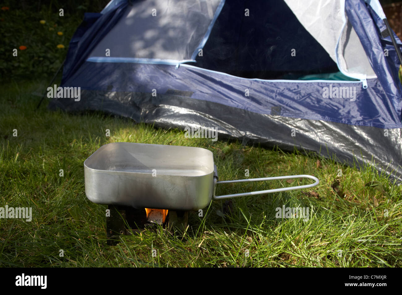 Piccola combustibile solido stufa utilizzata per riscaldare un pasticcio lo stagno di acqua nella parte anteriore della porta aperta di una tenda Foto Stock