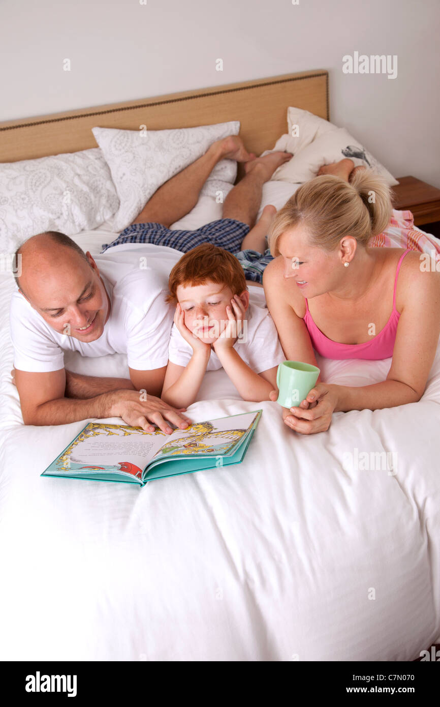 Famiglia di tre persone la lettura a letto insieme Foto Stock