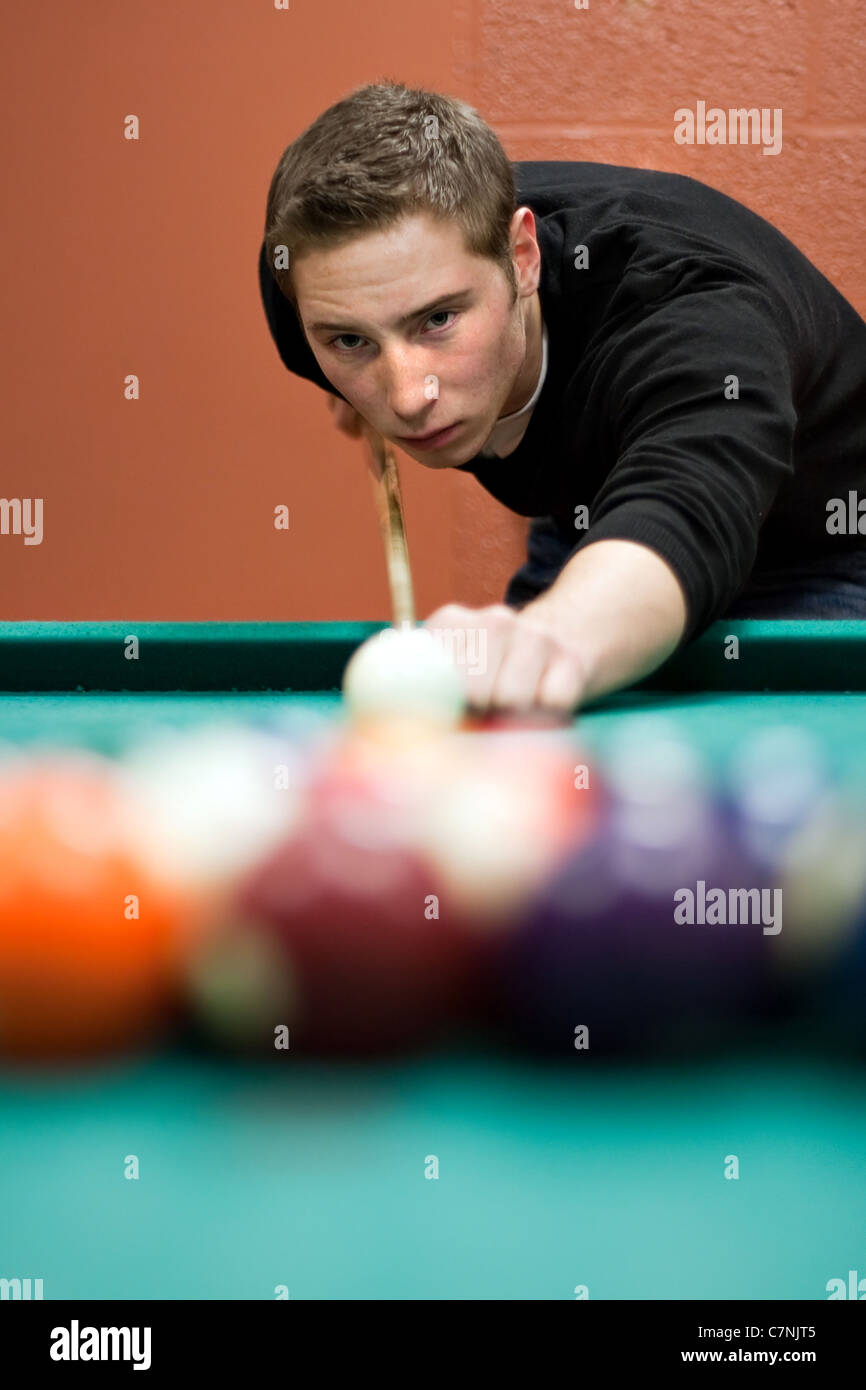 Un giovane uomo linee fino il suo tiro come egli rompe le sfere per l'inizio di un gioco di biliardo. Profondità di campo. Foto Stock