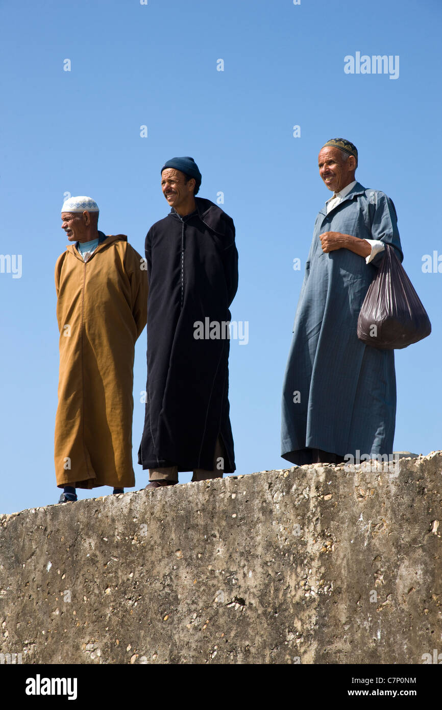 Tre Signori marocchino a guardare oltre le barche da pesca dal molo a Essaouira, Marocco Foto Stock