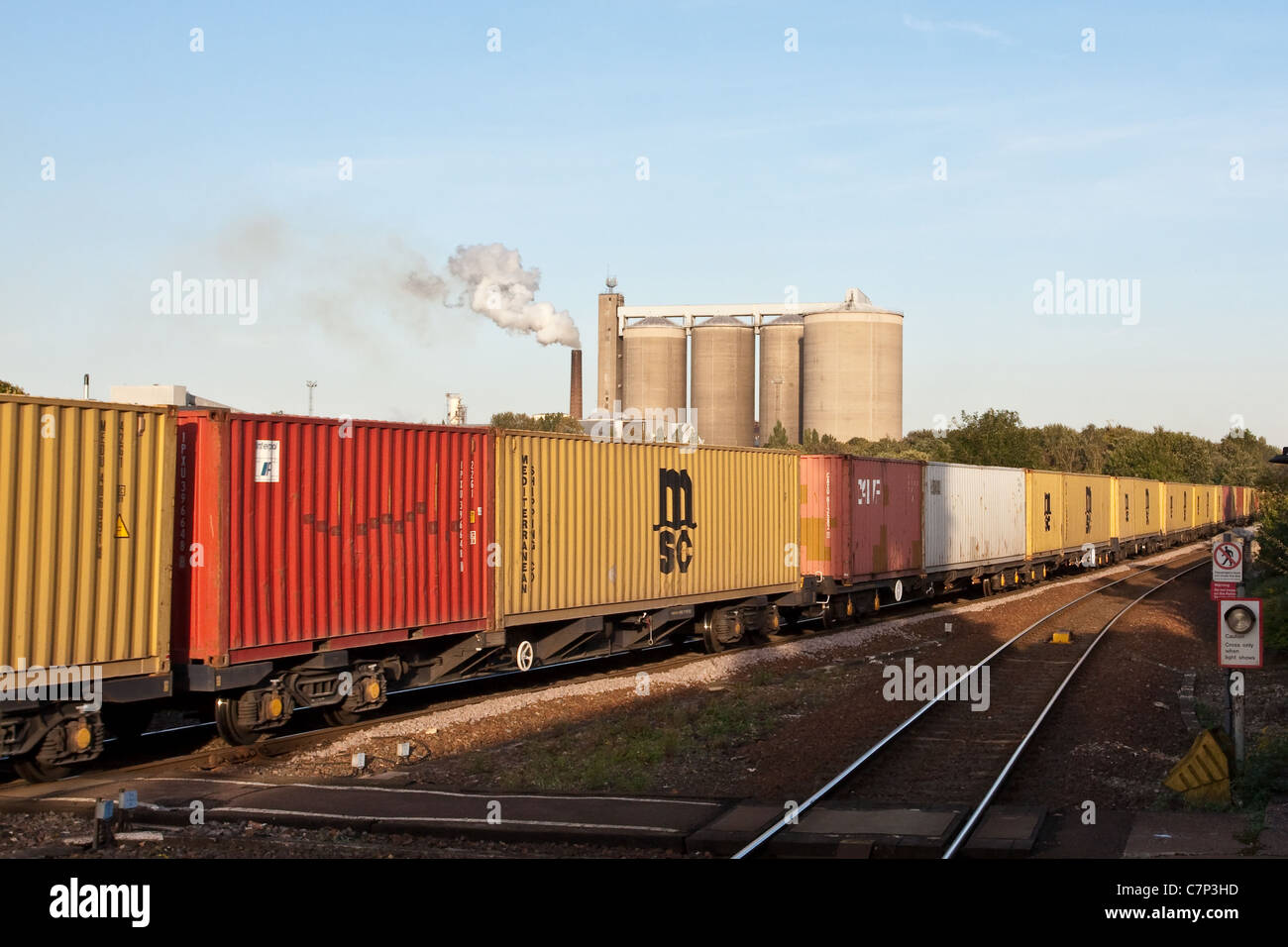 Treno merci viaggiano in direzione est a Bury St Edmunds stazione ferroviaria con la British Sugar Factory in background Foto Stock