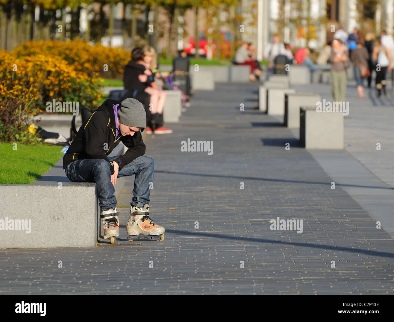 Ragazzo con lame a rullo seduto su una parete sul fiume Clyde marciapiede in Glasgow. Foto Stock
