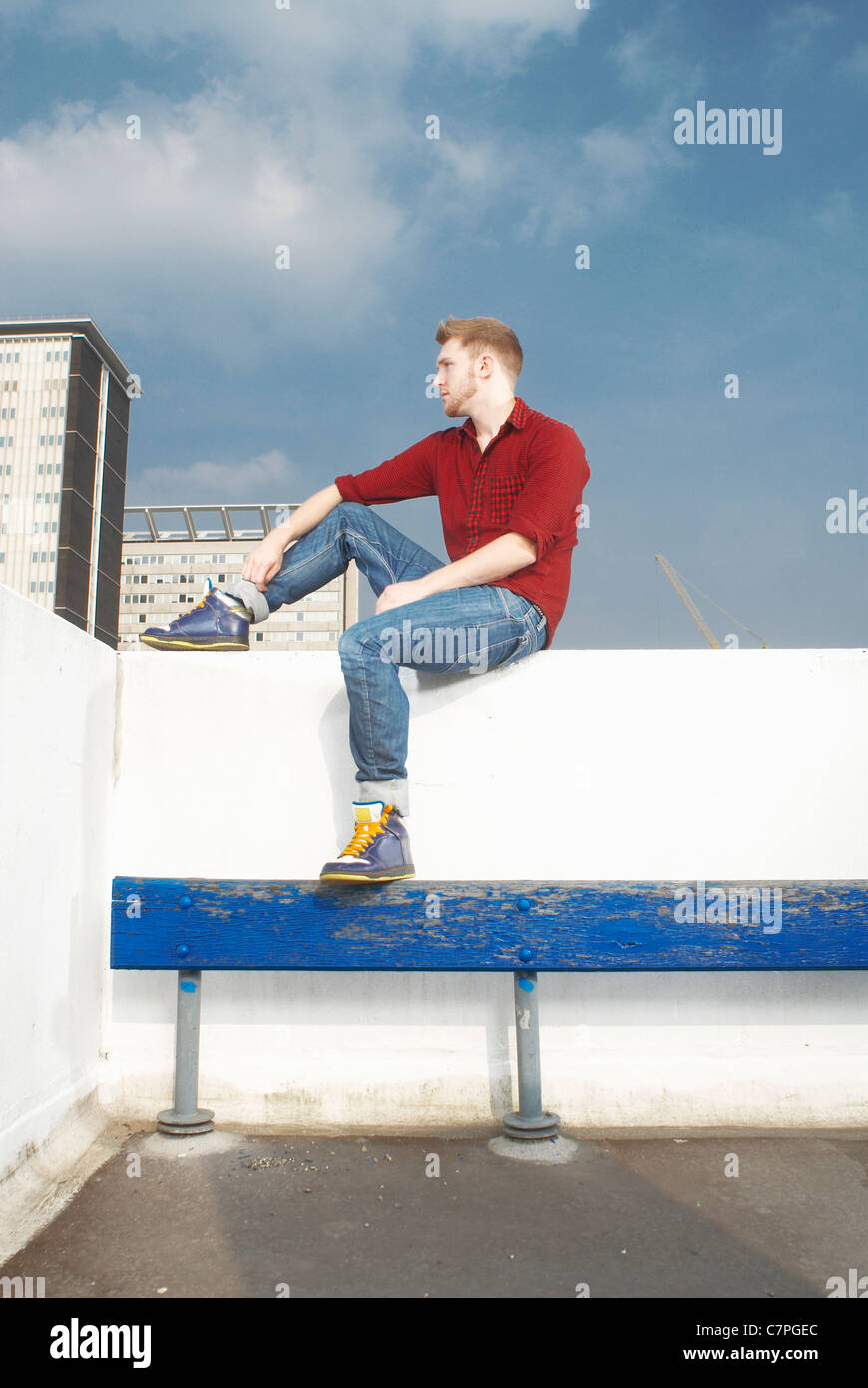 Uomo seduto sulla parete sul tetto Foto Stock