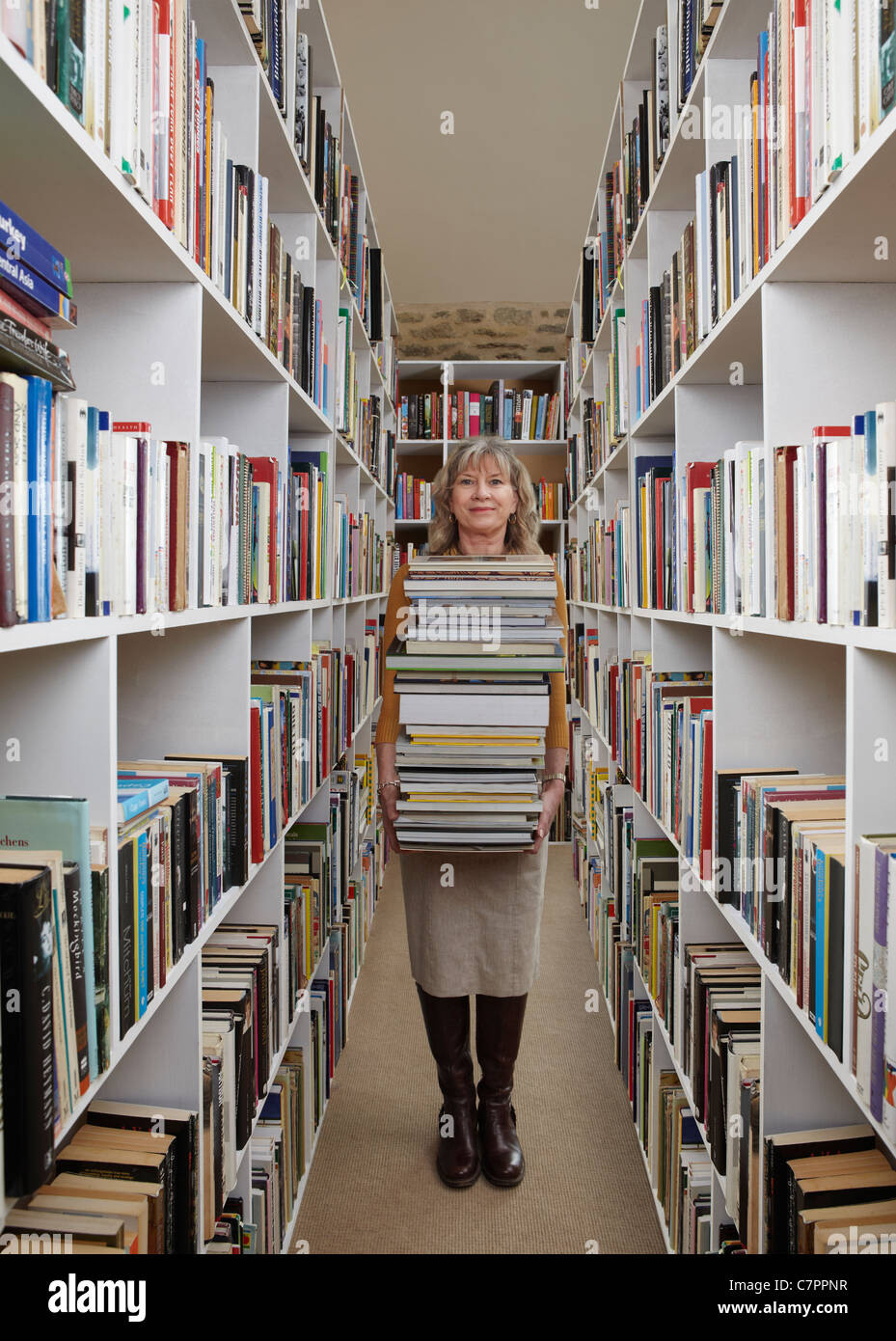 Donna anziana il trasporto di libri in biblioteca Foto Stock