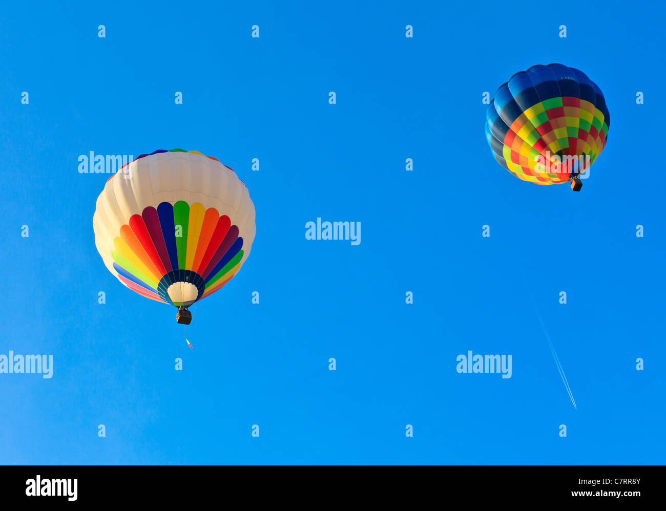 Due i palloni ad aria calda drifting su un cielo blu con una coda bianca da un aeroplano a distanza Foto Stock