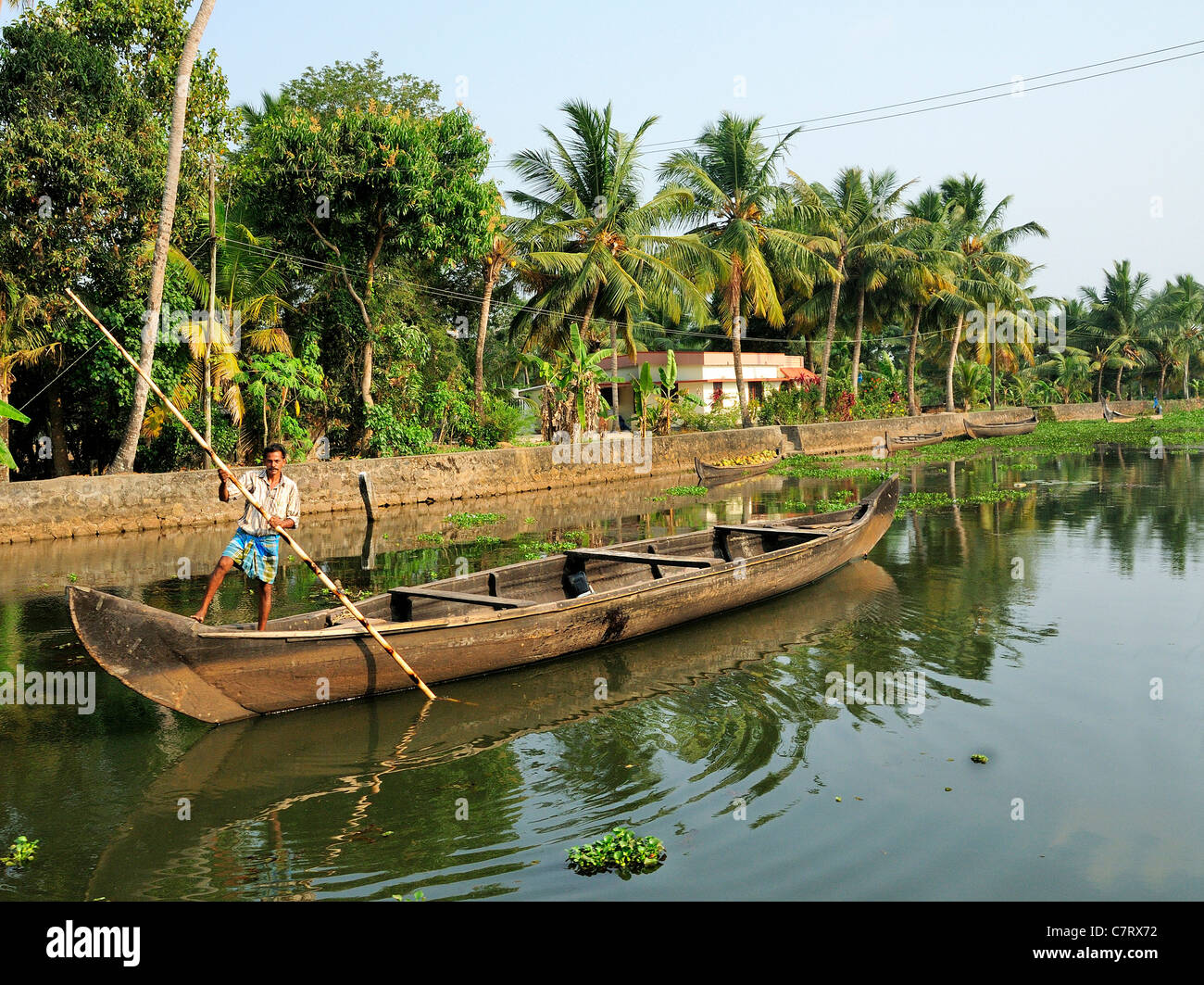Uomo che punisce la sua canoa da lavoro vuota, un vallam, lungo un fiume nelle acque arretrate del Kerala, India meridionale, India Foto Stock