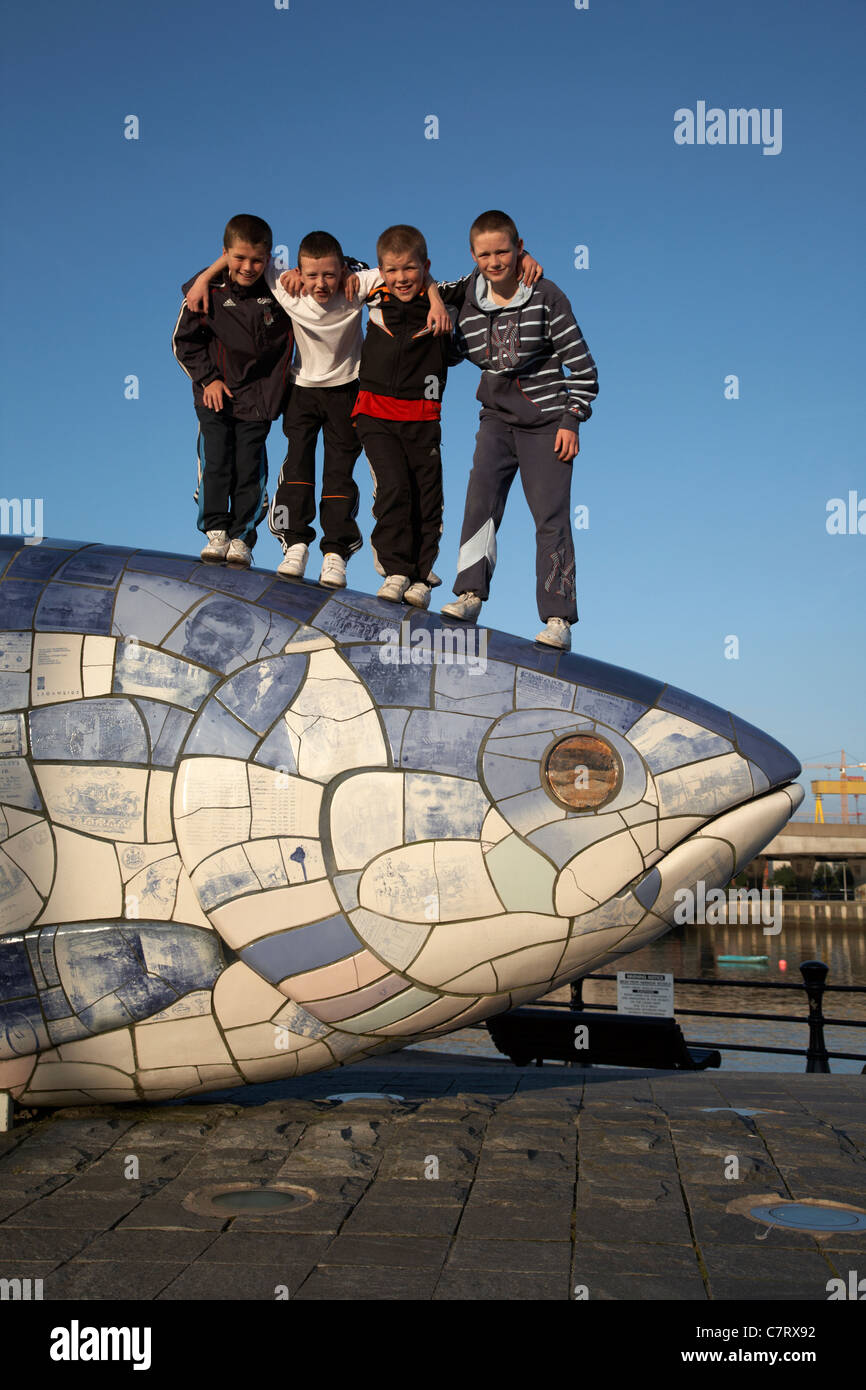 Locali di bambini che giocano su "Il grande pesce' scultura di salmone da John gentilezza accanto al fiume Lagan in Belfast City Centre Foto Stock