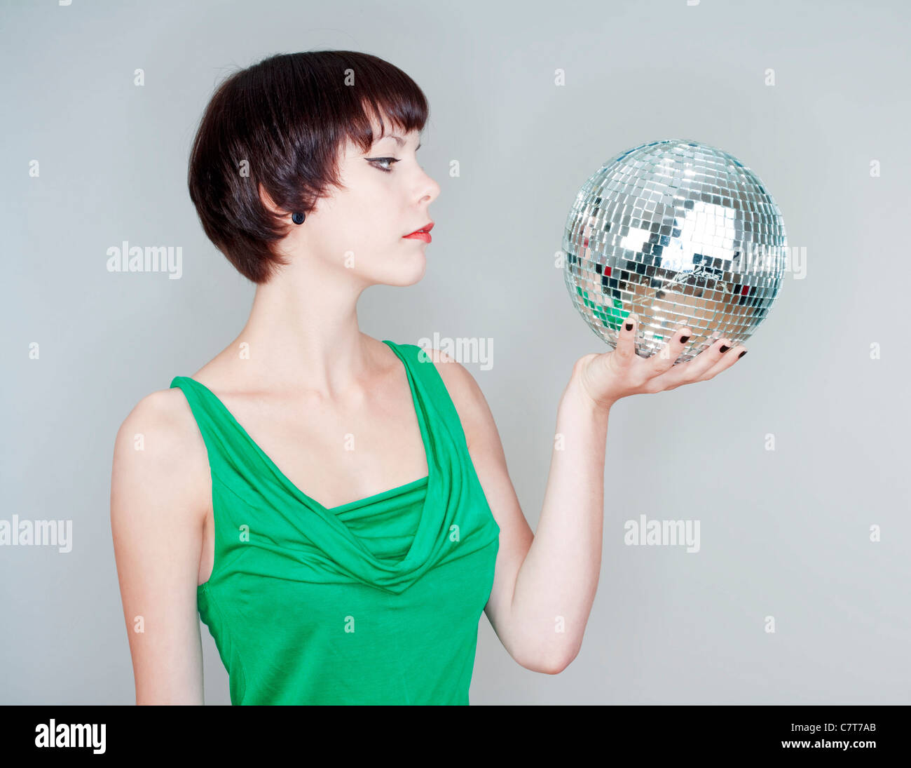 Giovane donna tenendo una palla da discoteca cercando - isolato su grigio Foto Stock