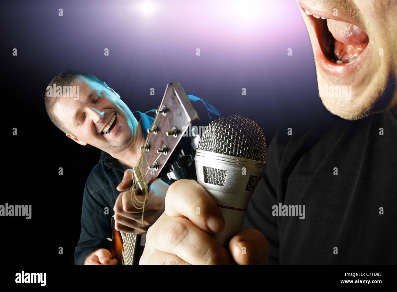 Due interpreti con microfono e chitarra su sfondo nero Foto Stock