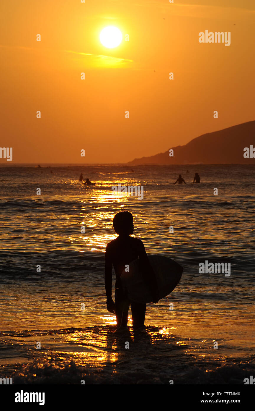 Un giovane maschio surfer orologi il tramonto a Bantham beach nel Devon verso la fine di settembre. Foto Stock