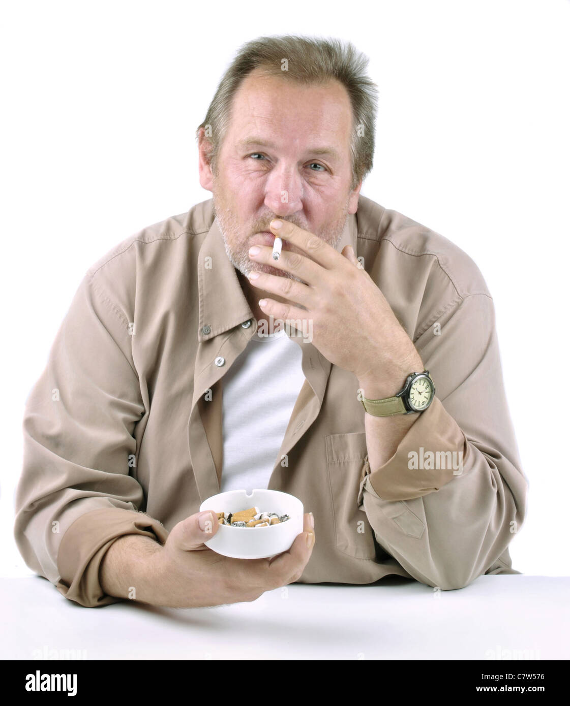 Inorridita l uomo nella sua 50s seduti ad un tavolo con una sigaretta e posacenere Foto Stock