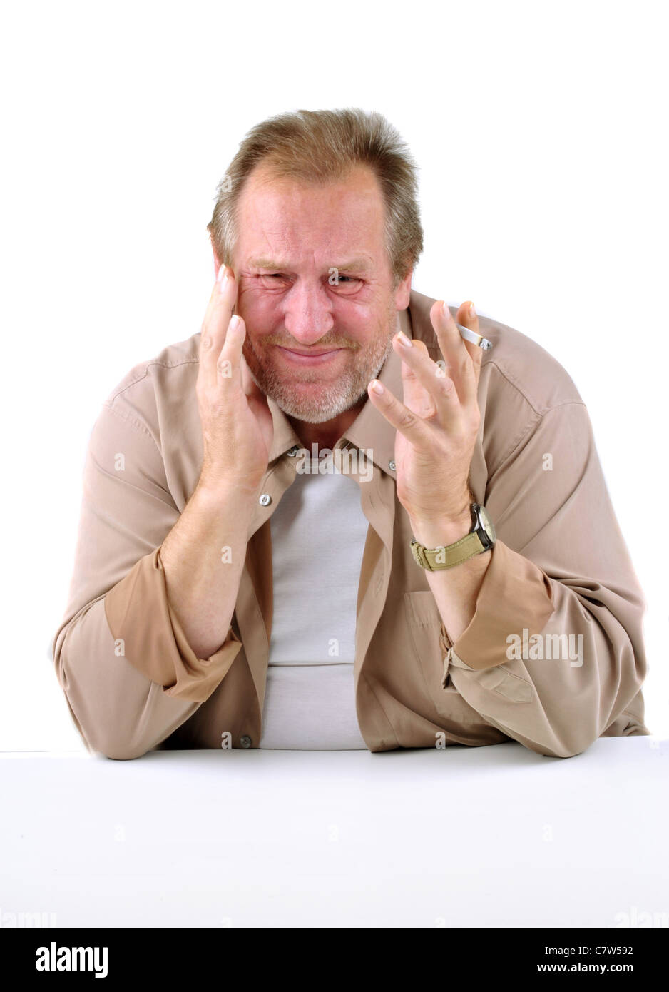 Inorridita l uomo nella sua 50s seduti ad un tavolo con una sigaretta Foto Stock