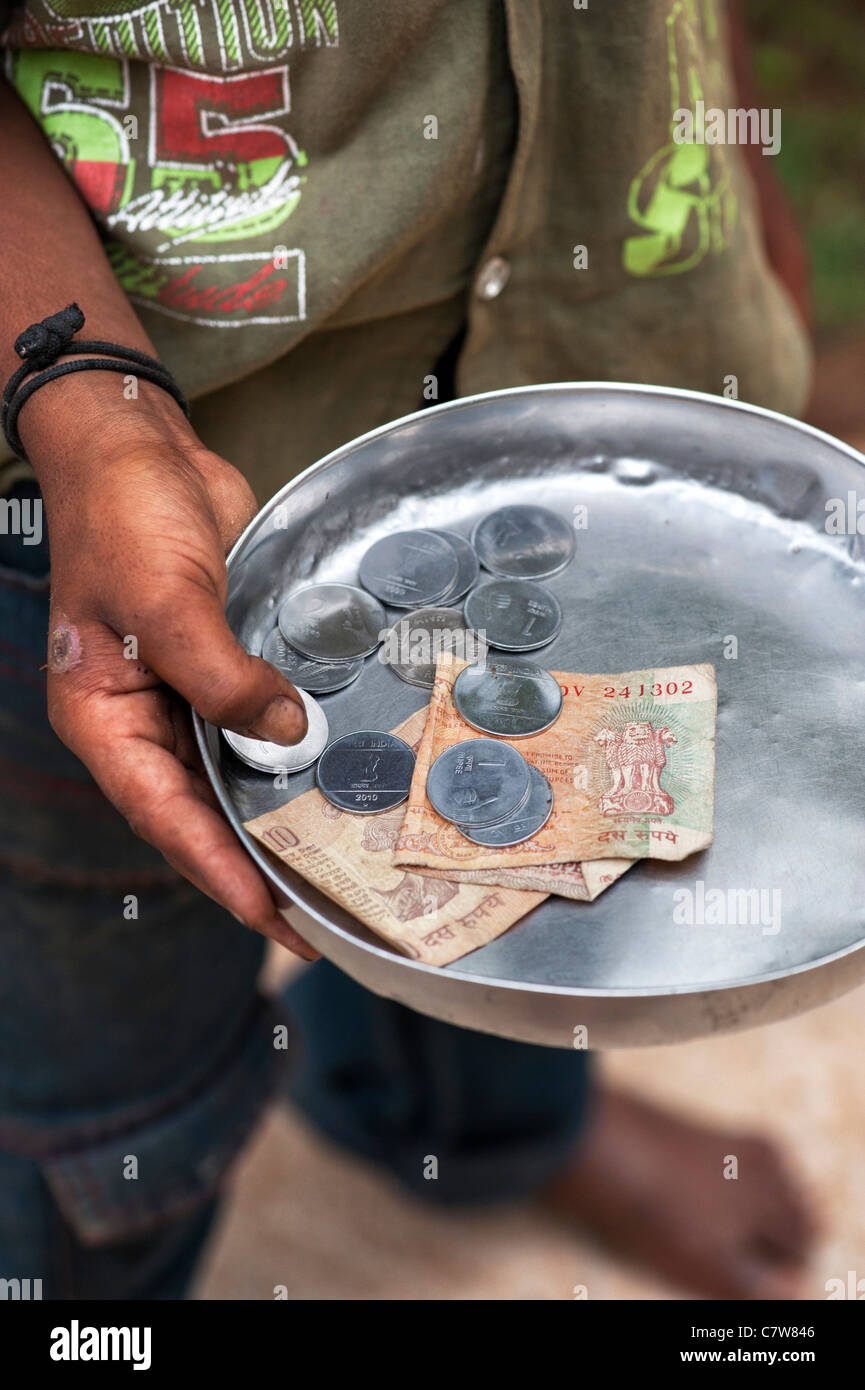 I giovani poveri di casta inferiore indiano ragazzo di strada mendicando con piastra di denaro. Andhra Pradesh, India. Il fuoco selettivo Foto Stock